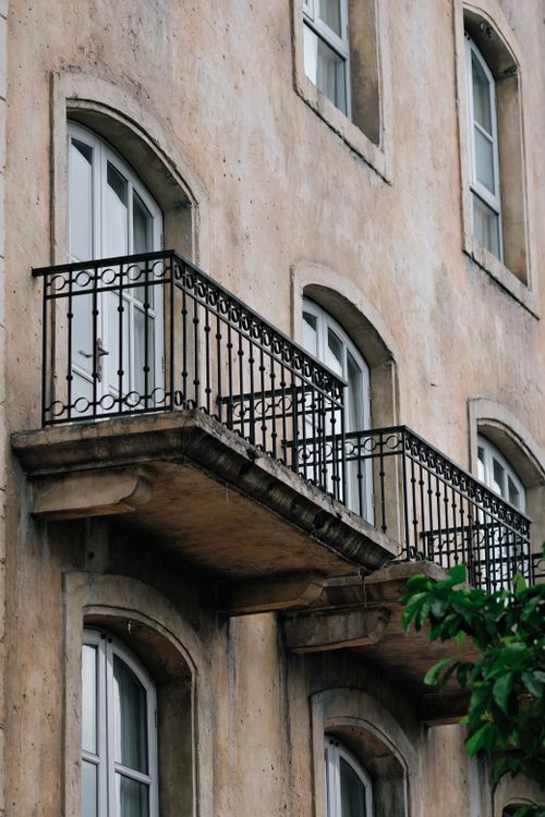 Free Weathered building facade with ornate iron balcony and arched windows. Stock Photo