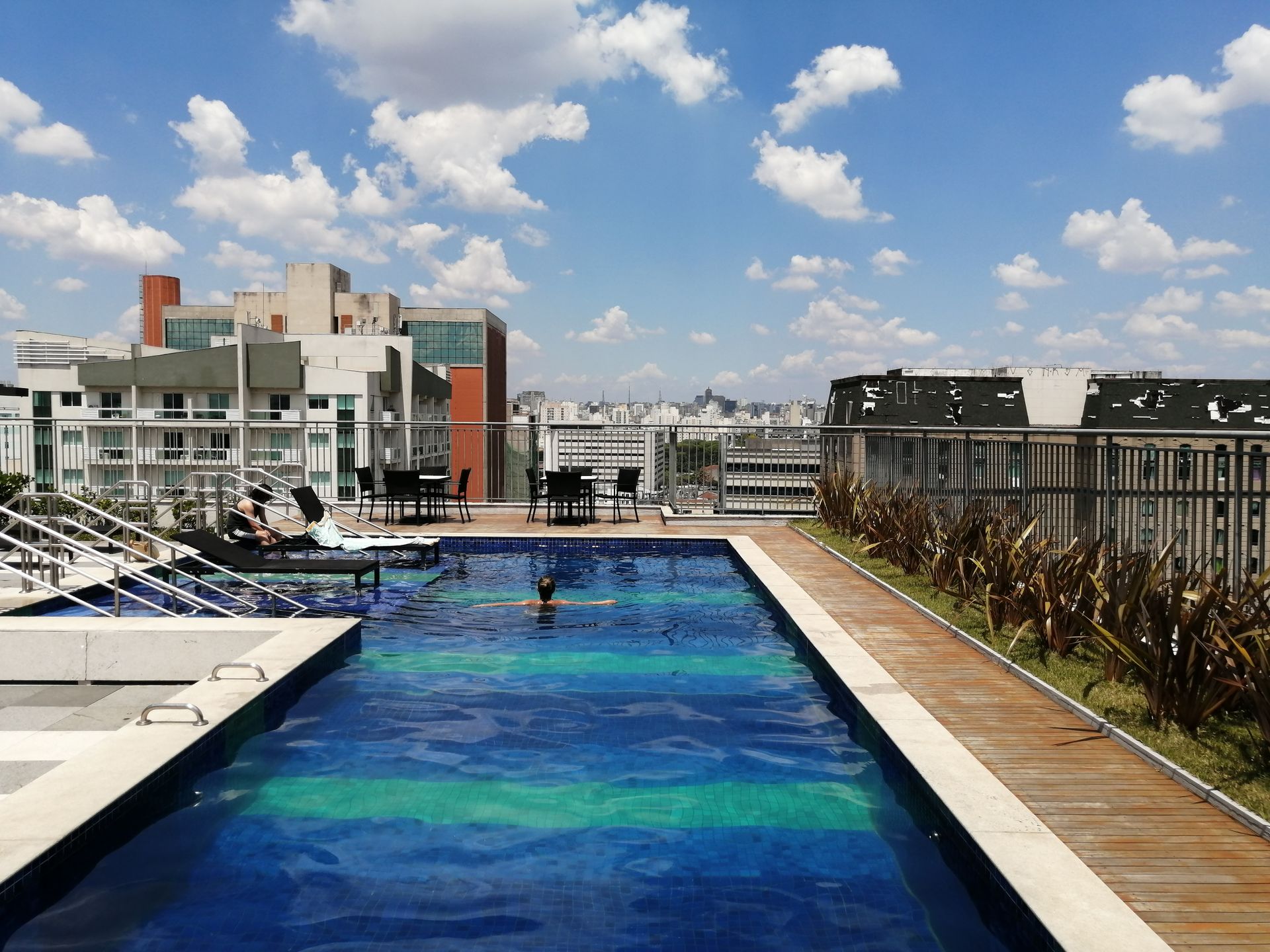 A serene rooftop pool with a view of São Paulo's skyline under a clear blue sky, offering a relaxing urban escape.