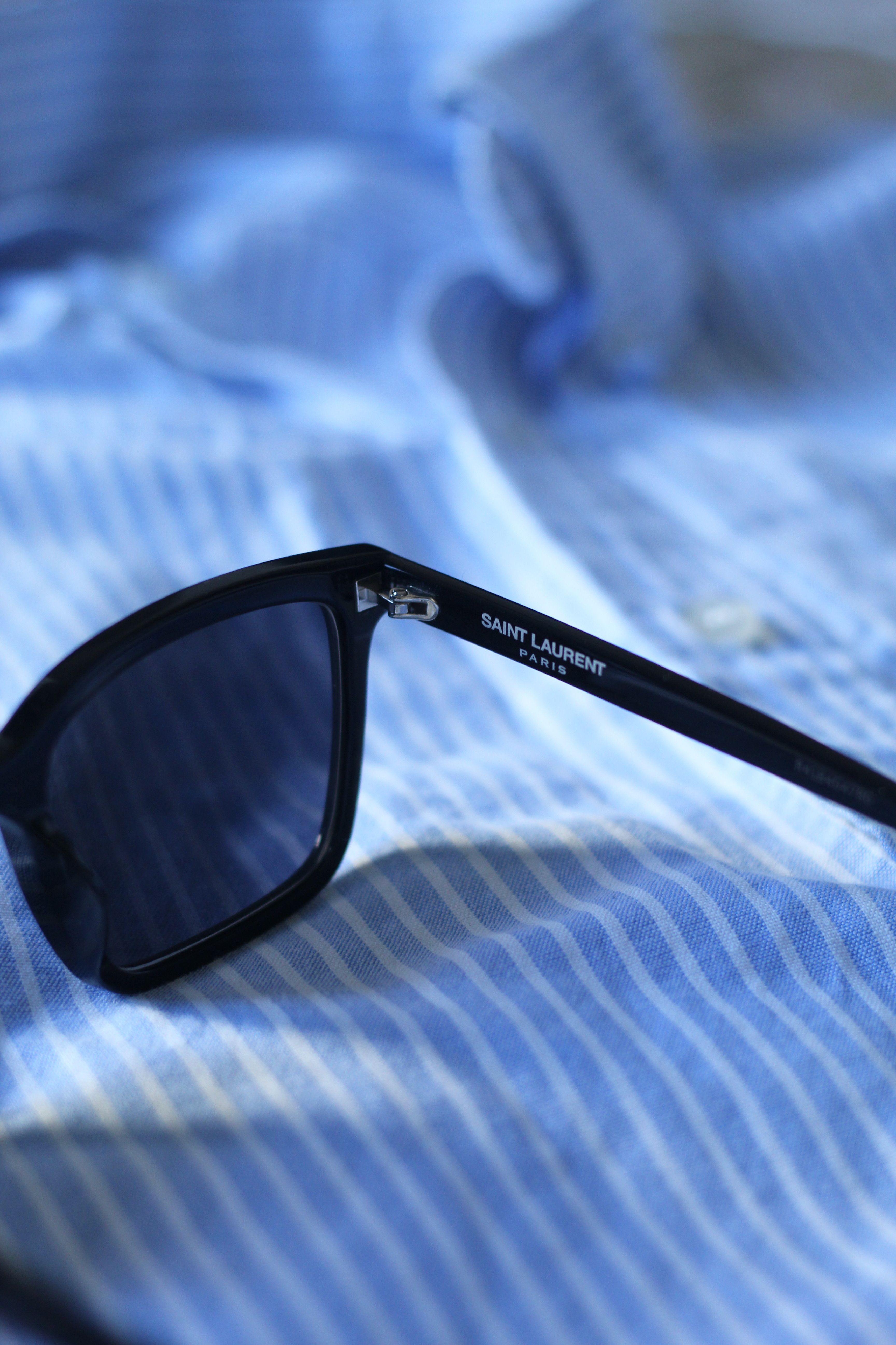 Stylish black sunglasses resting on a light blue striped shirt, perfect for a summer look.