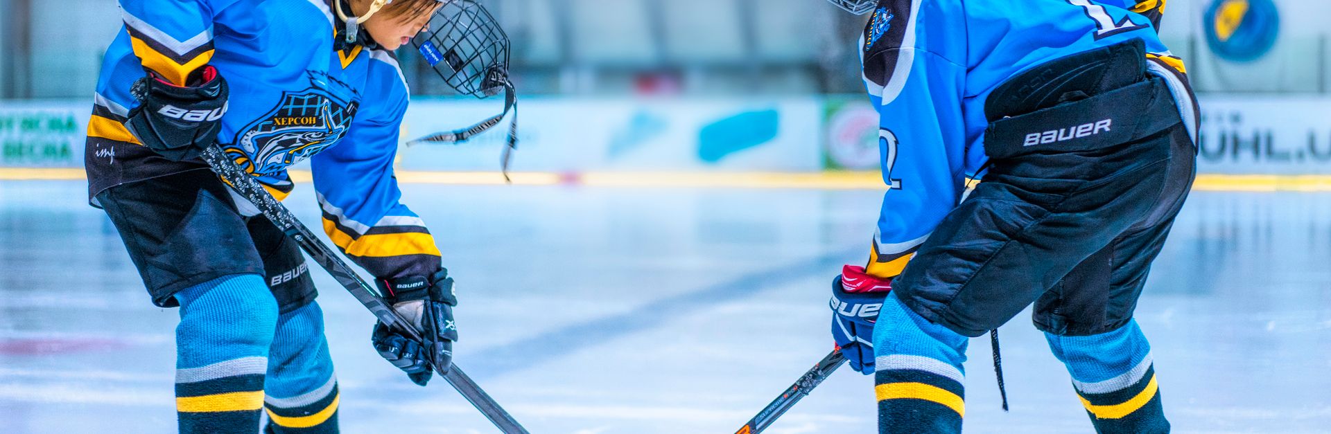 Two young athletes face-off during an ice hockey game in an indoor rink.