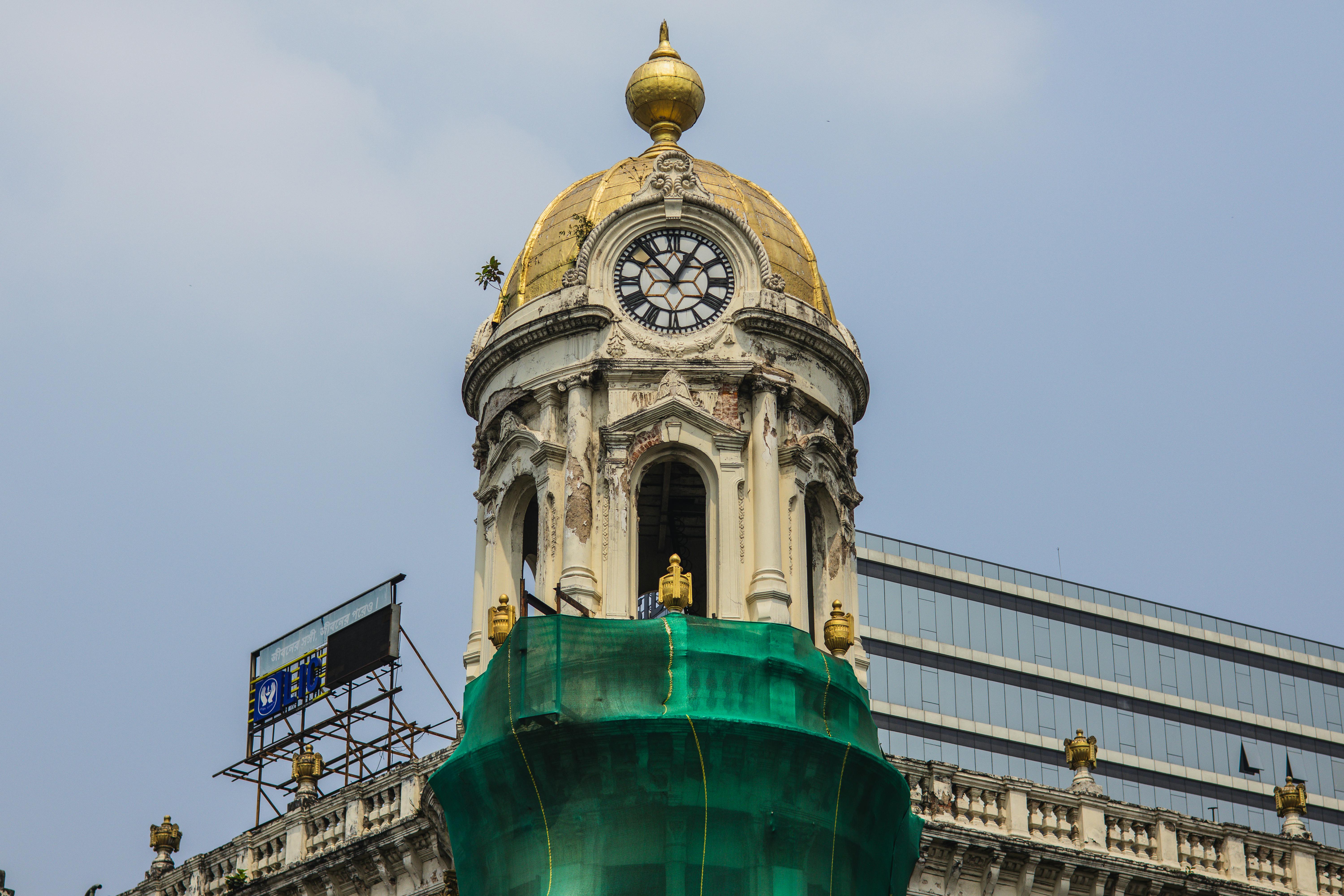 A historic clock tower with a golden dome undergoing renovation against a clear blue sky.