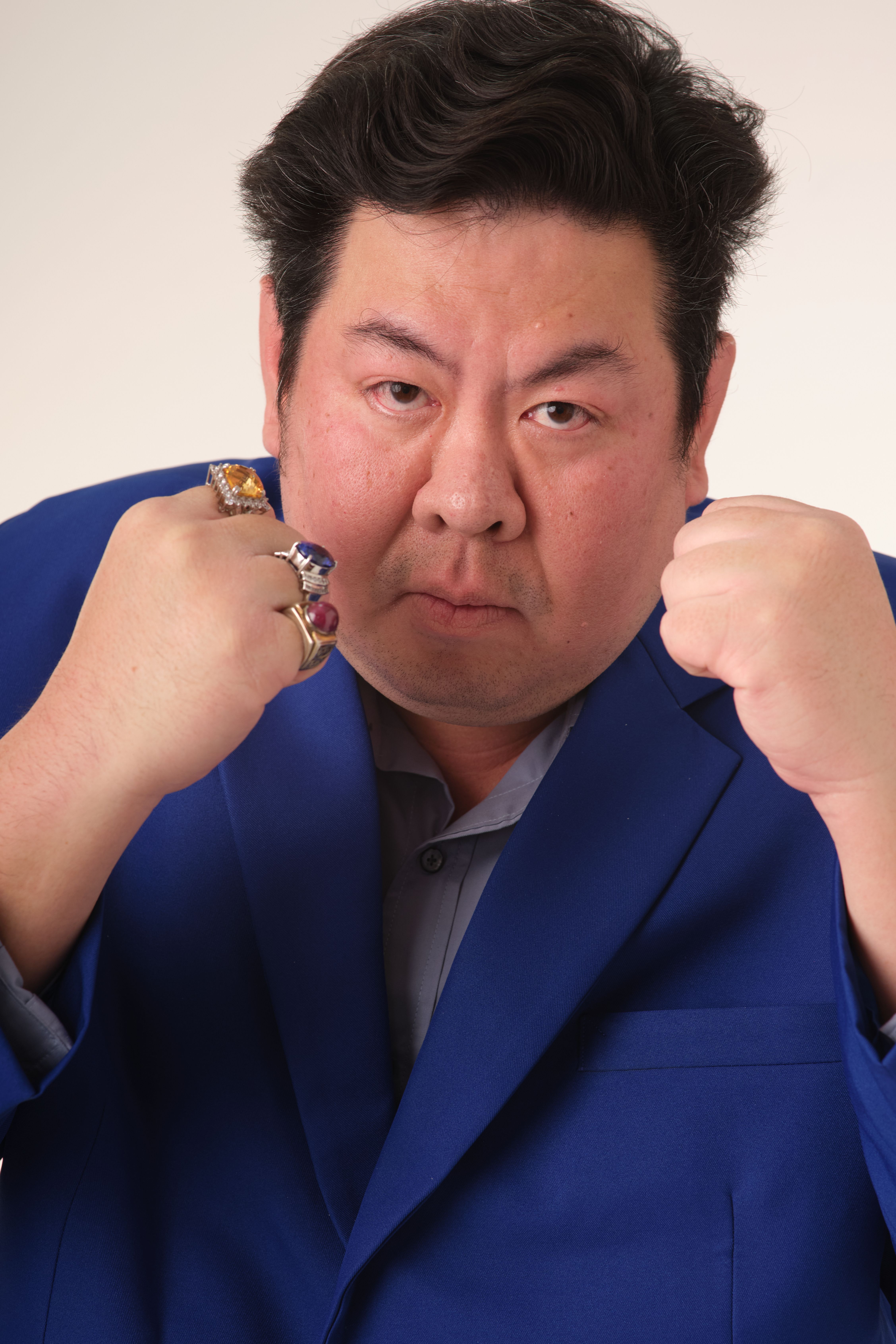 Confident man with rings in blue suit striking a defensive pose indoors.