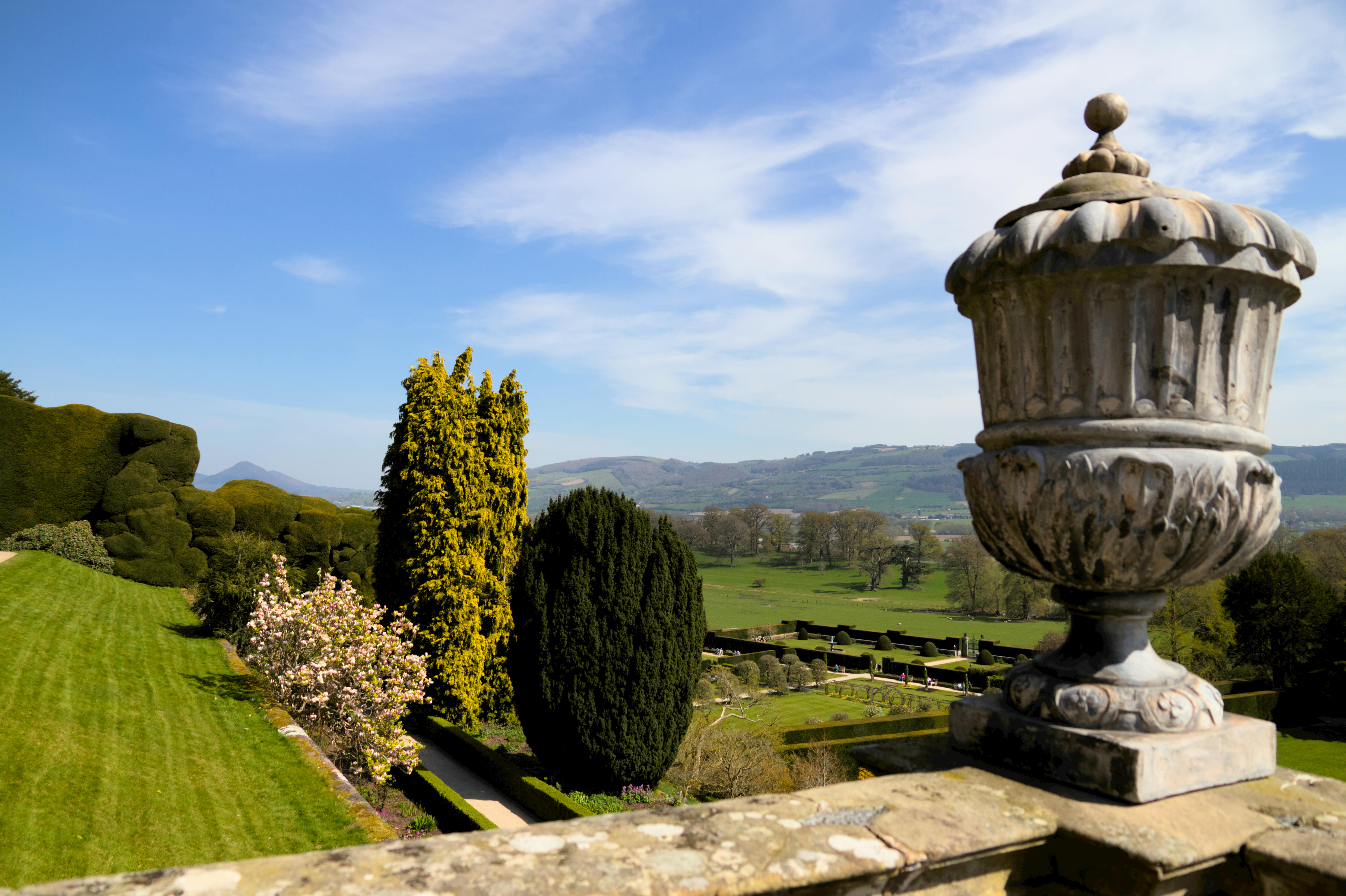 Un magnifique jardin avec une urne en pierre donne sur une vue pittoresque sur la campagne, incarnant la beauté tranquille de l'extérieur.