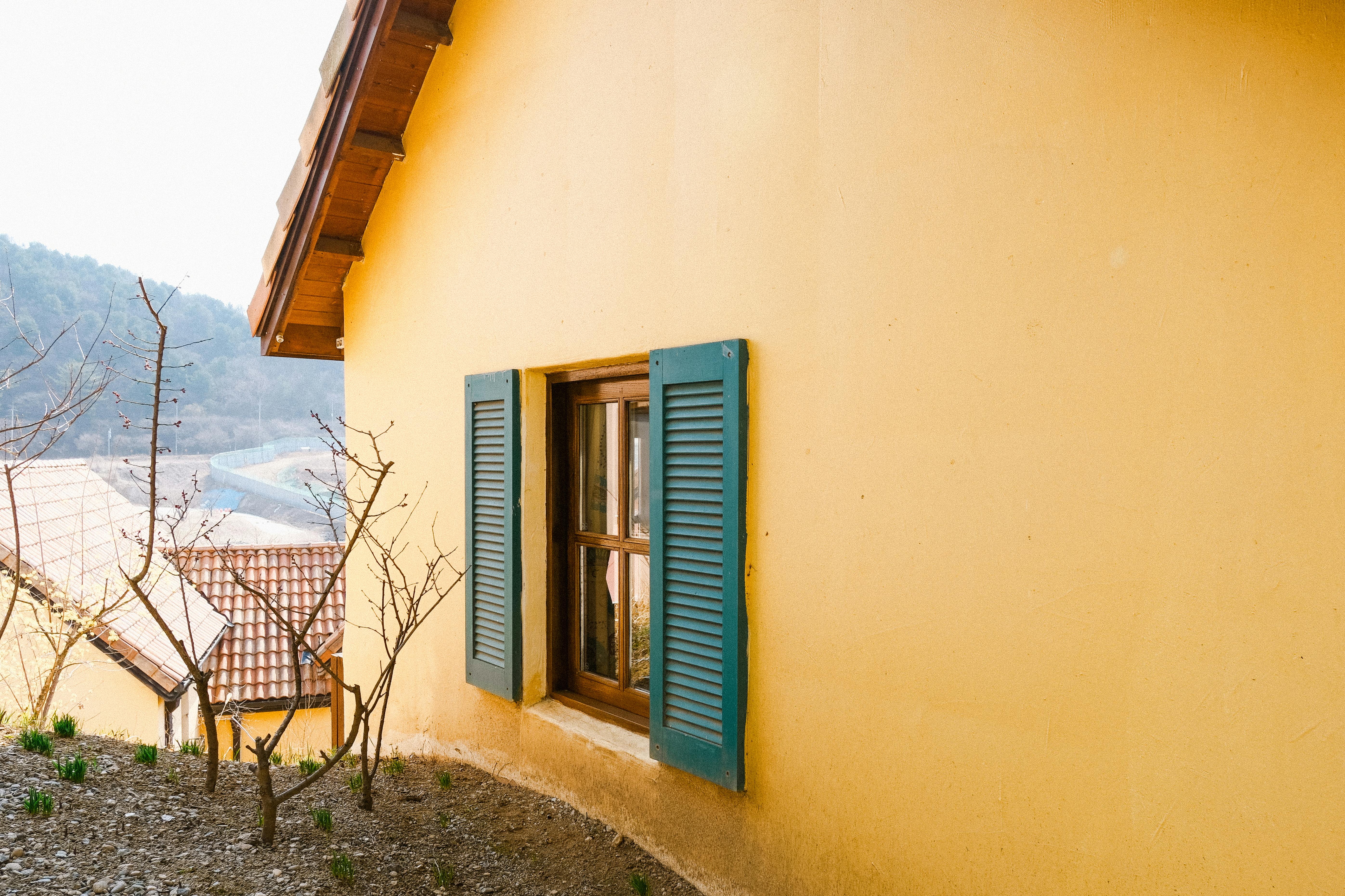 A picturesque yellow house with blue shutters in a serene rural setting.