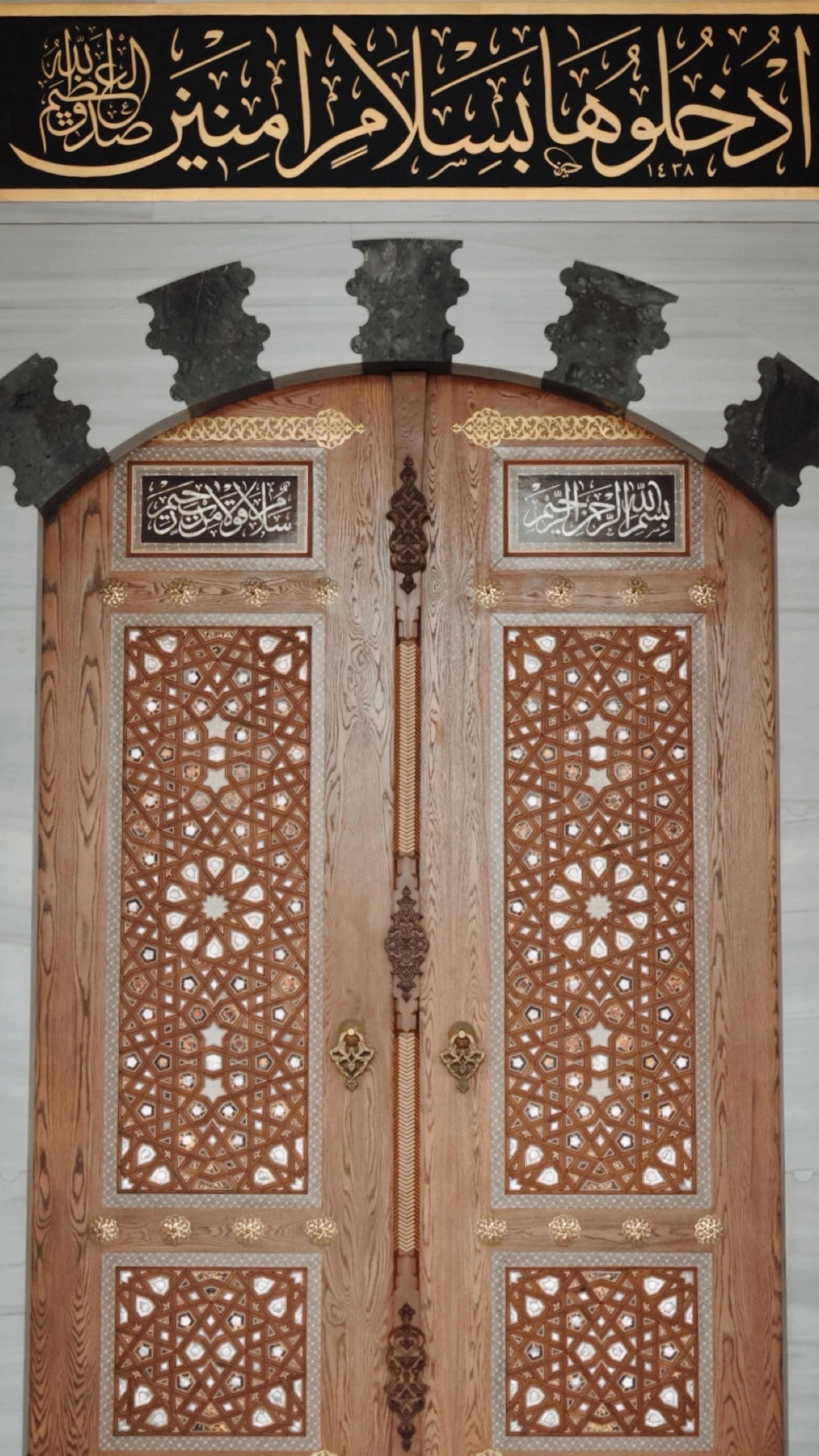 A beautifully carved wooden door adorned with Arabic calligraphy and ornate patterns, showcasing Islamic architecture.