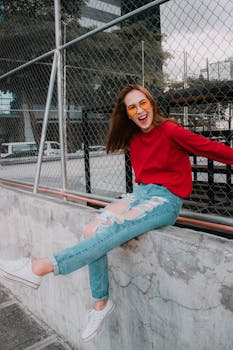 一位穿着红色毛衣和破洞牛仔裤的女人，正坐在栅栏上，享受着阳光明媚的日子