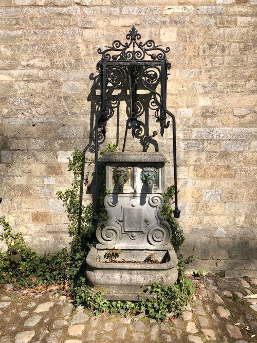 Free A decorative stone fountain with intricate metalwork in a sunny courtyard, surrounded by ivy. Stock Photo