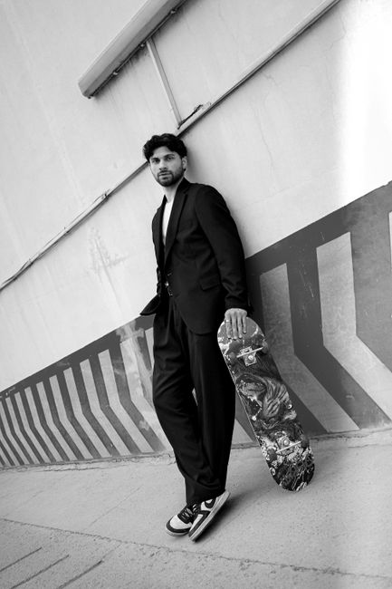 Urban fashion portrait of a man with a skateboard by a geometric patterned wall.