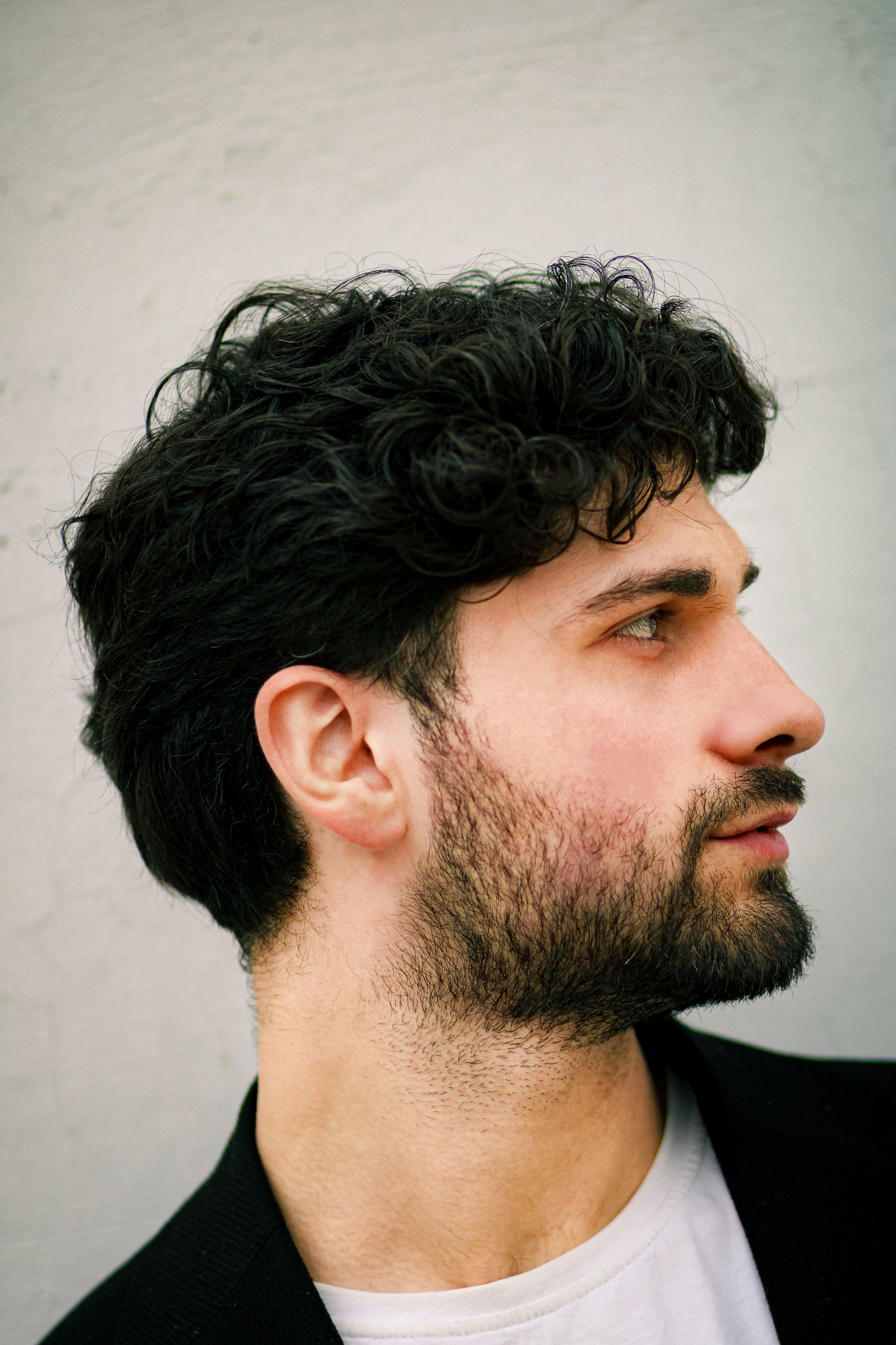 Side profile portrait of a young man with curly hair, beard, and a pensive look.