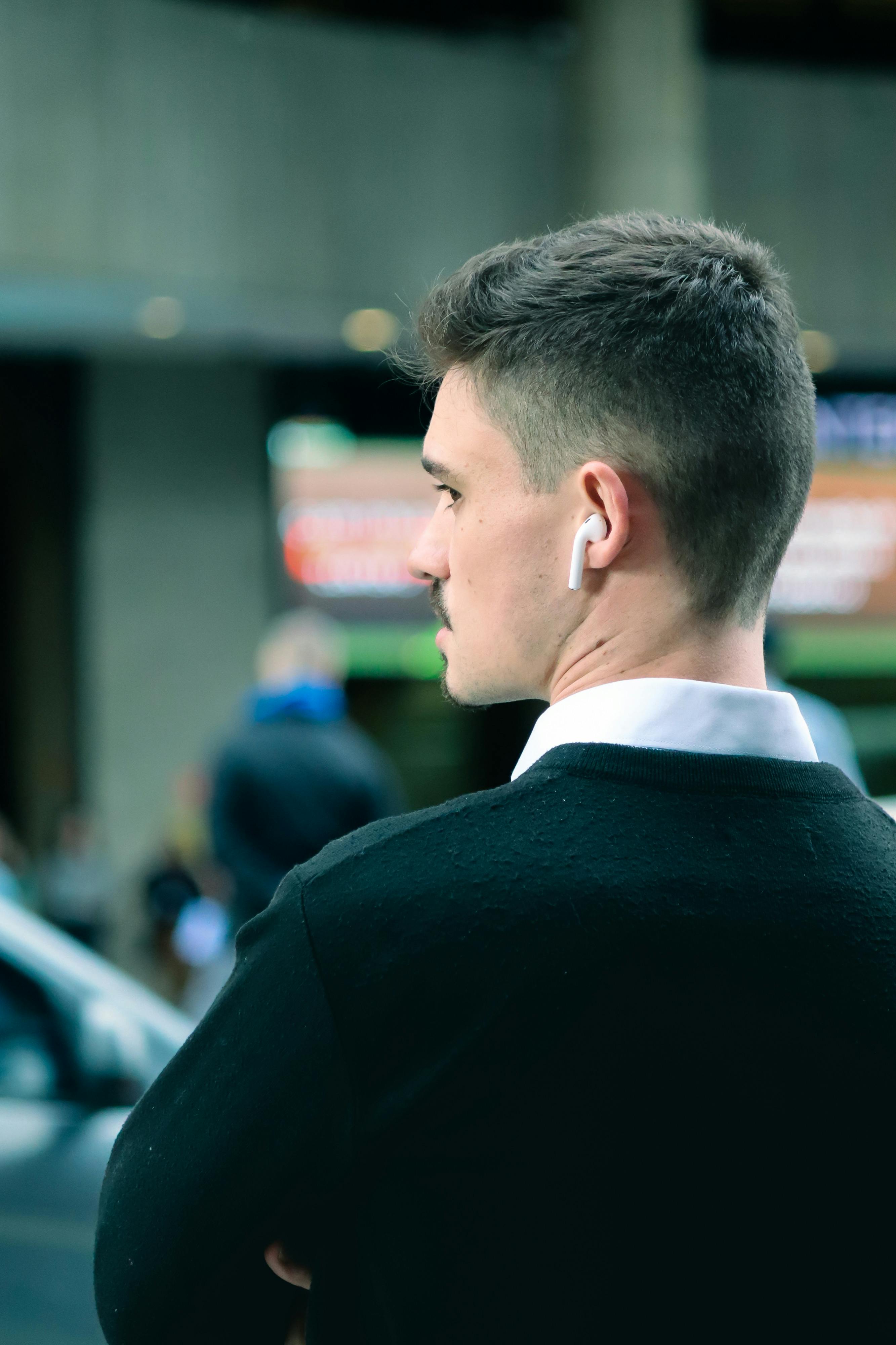 免費 一名男子在城市環境中戴著無線耳機，若有所思，注意力集中。 圖庫相片