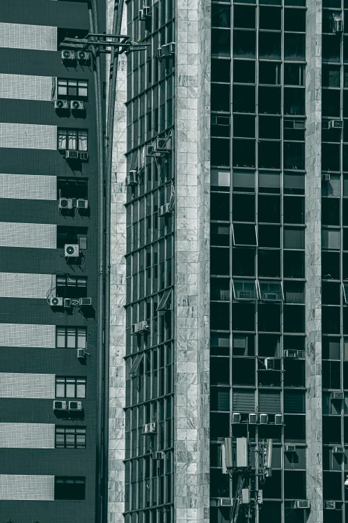 Free Close-up of a multi-story modern building facade featuring air conditioners and glass windows. Stock Photo