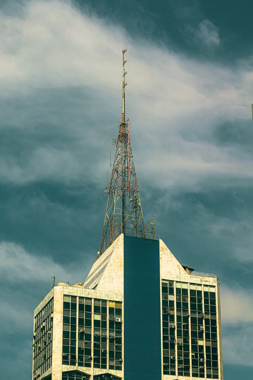 Free Skyscraper with antenna on top against a dramatic sky, showcases urban architecture. Stock Photo