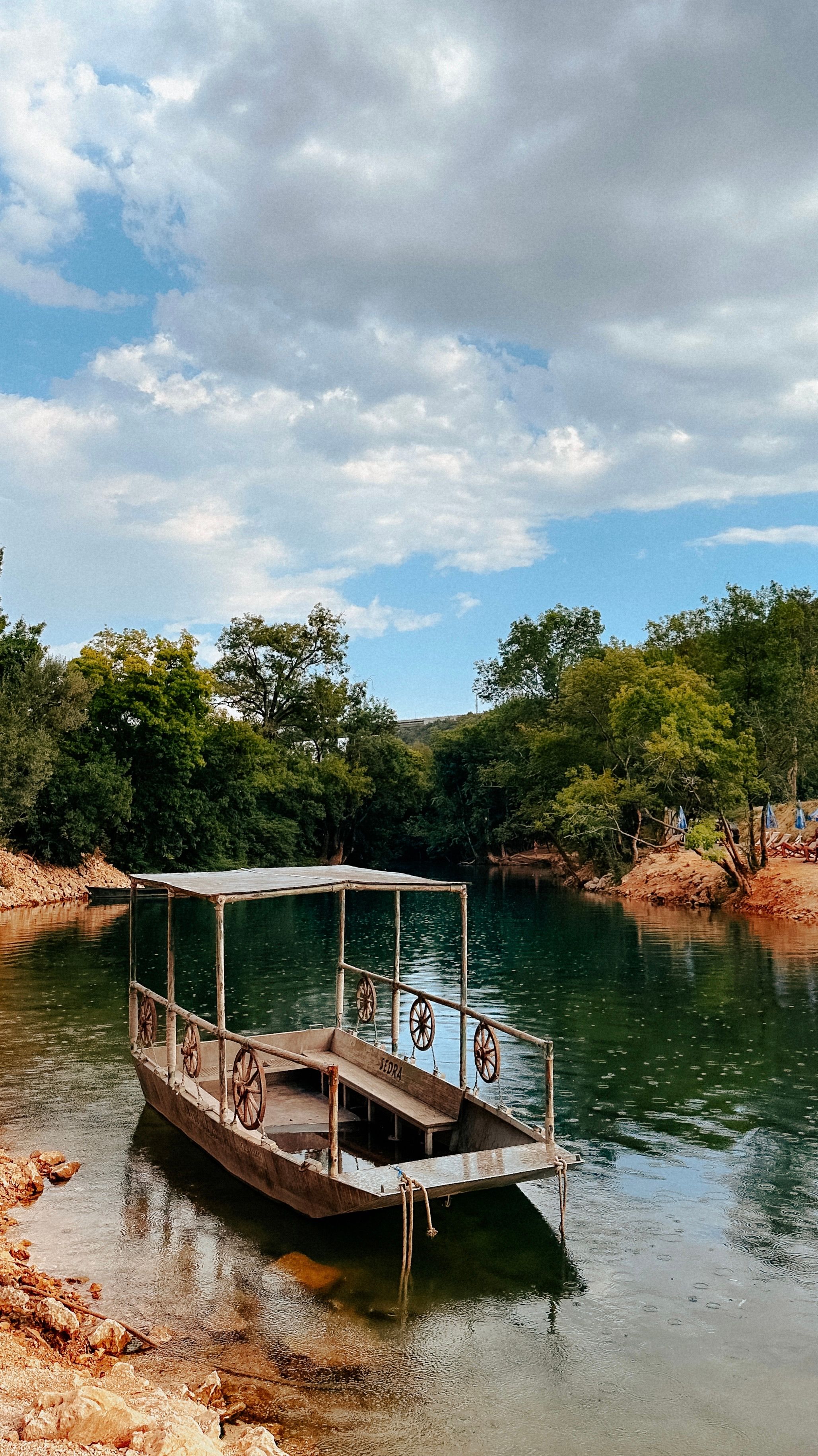 Peaceful river scene with a rustic boat in Studenci, Bosnia. Ideal for travel and nature themes.