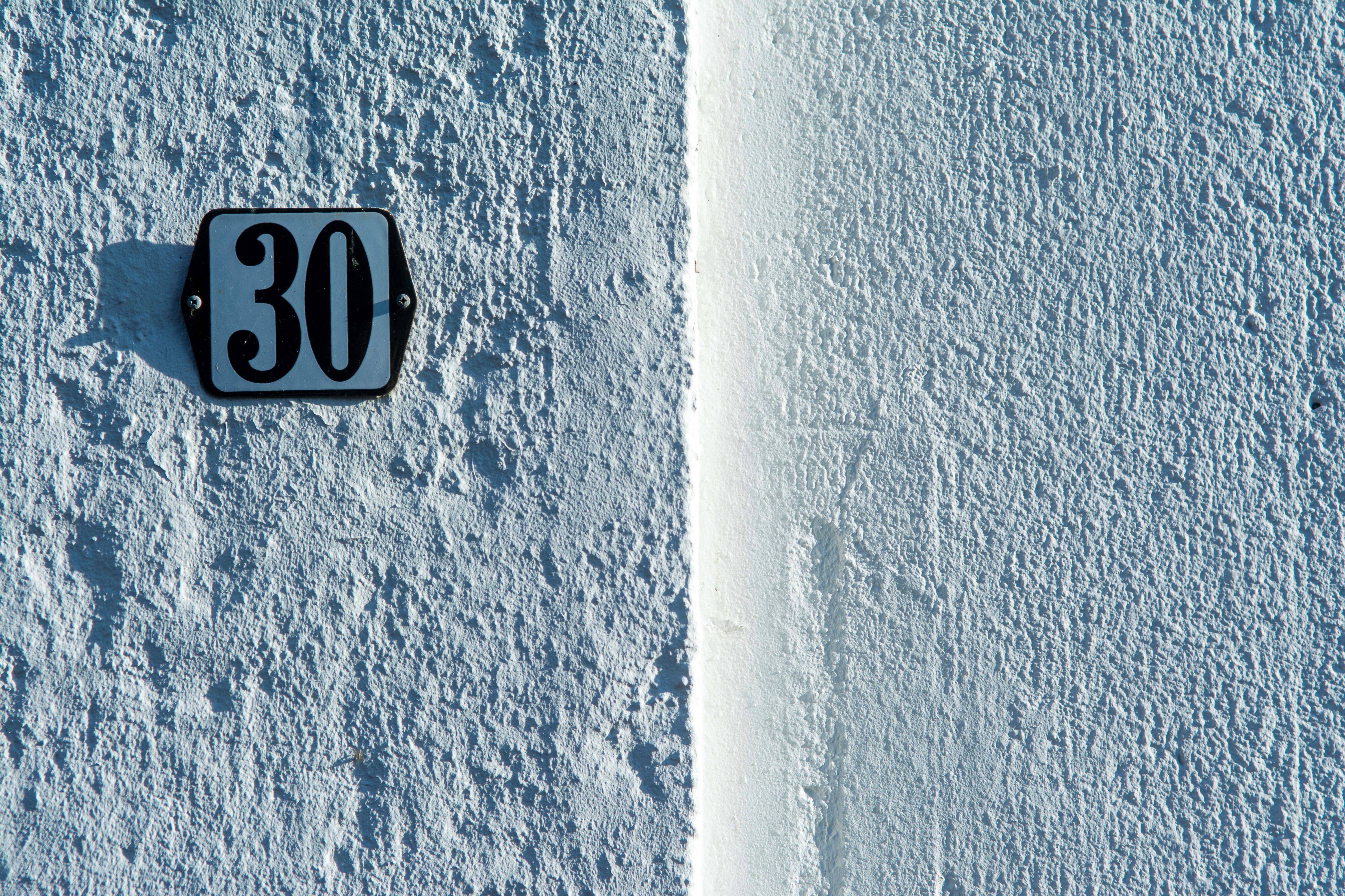 Gratis Primo piano di una parete bianca ruvida con un classico cartello con il numero civico 30. Foto a disposizione