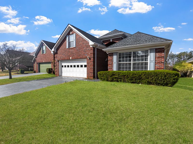 Red brick suburban house with a well-kept lawn under a clear blue sky