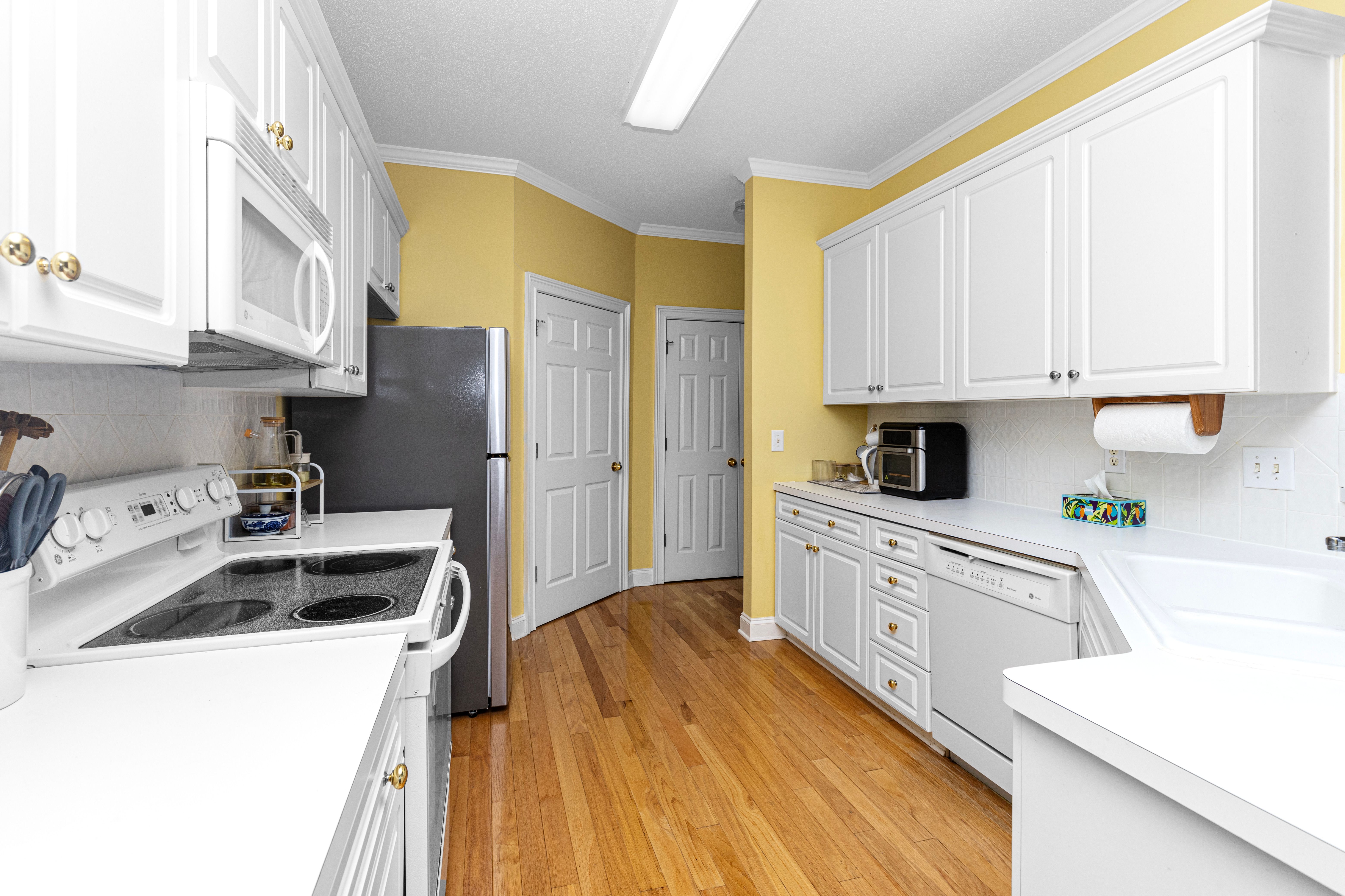 Free Spacious kitchen with white cabinets, wooden floor, and modern appliances. Stock Photo