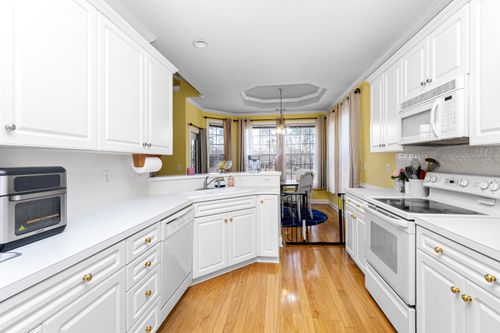 Free Bright modern kitchen with white cabinets, wooden floors, and stainless steel appliances. Stock Photo