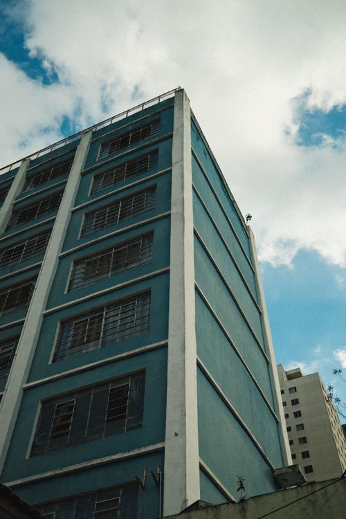 Free A towering urban high-rise building with a blue facade set against a bright, cloudy sky. Stock Photo