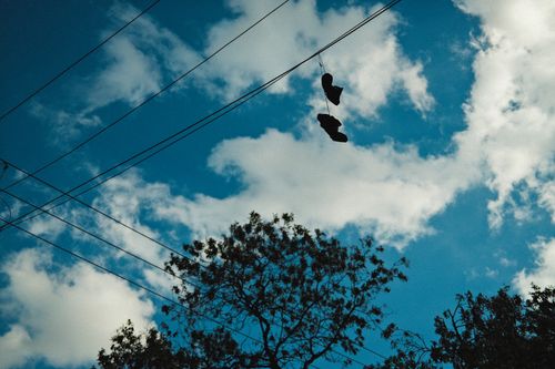 Free A pair of shoes hanging over power lines with a backdrop of a clear blue sky and scattered clouds. Stock Photo