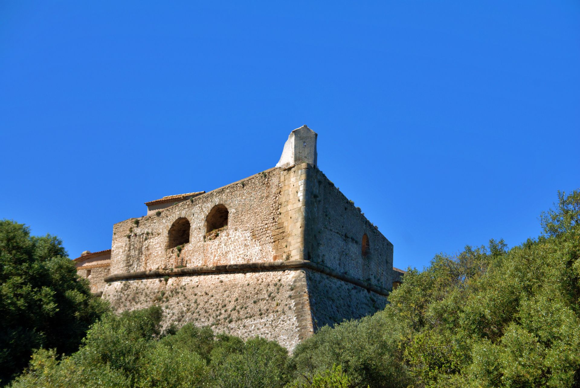 Scenic view of the ancient Fort Carré in Antibes, framed by greenery and clear blue skies.