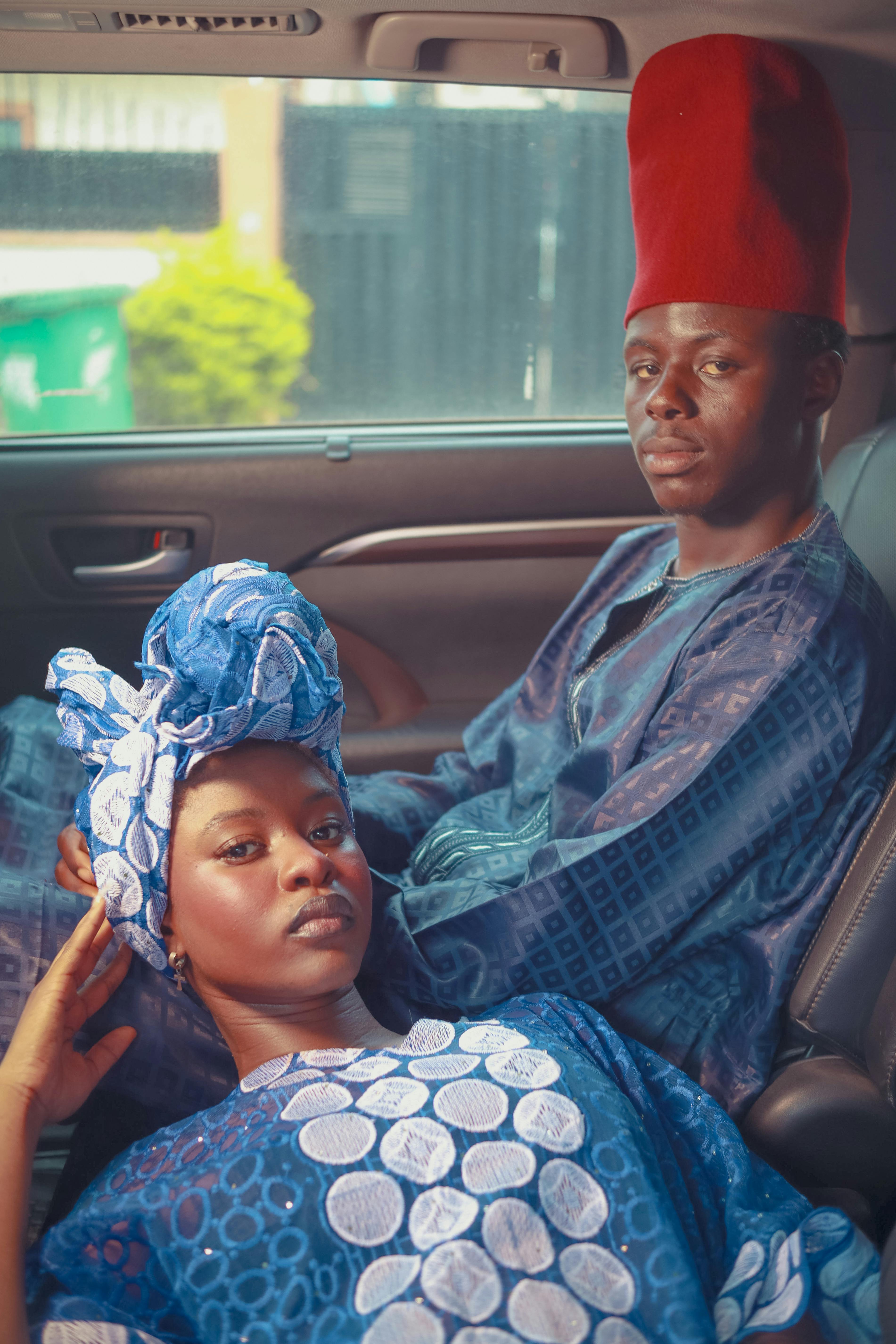 African couple in a car wearing stylish traditional attire and distinctive headgear.