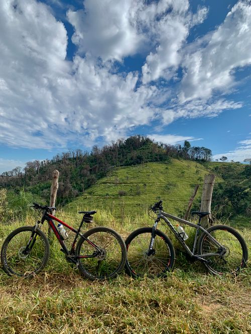 Free Two mountain bikes resting on a grassy hillside with a scenic view of hills and cloudy sky. Stock Photo