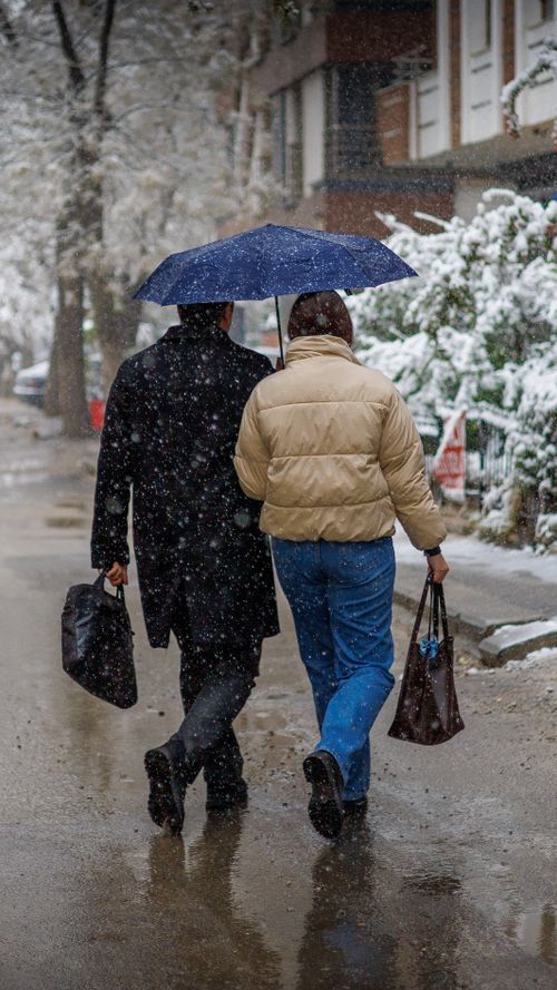Free Two people walking with an umbrella on a snowy city street capturing winter urban life. Stock Photo