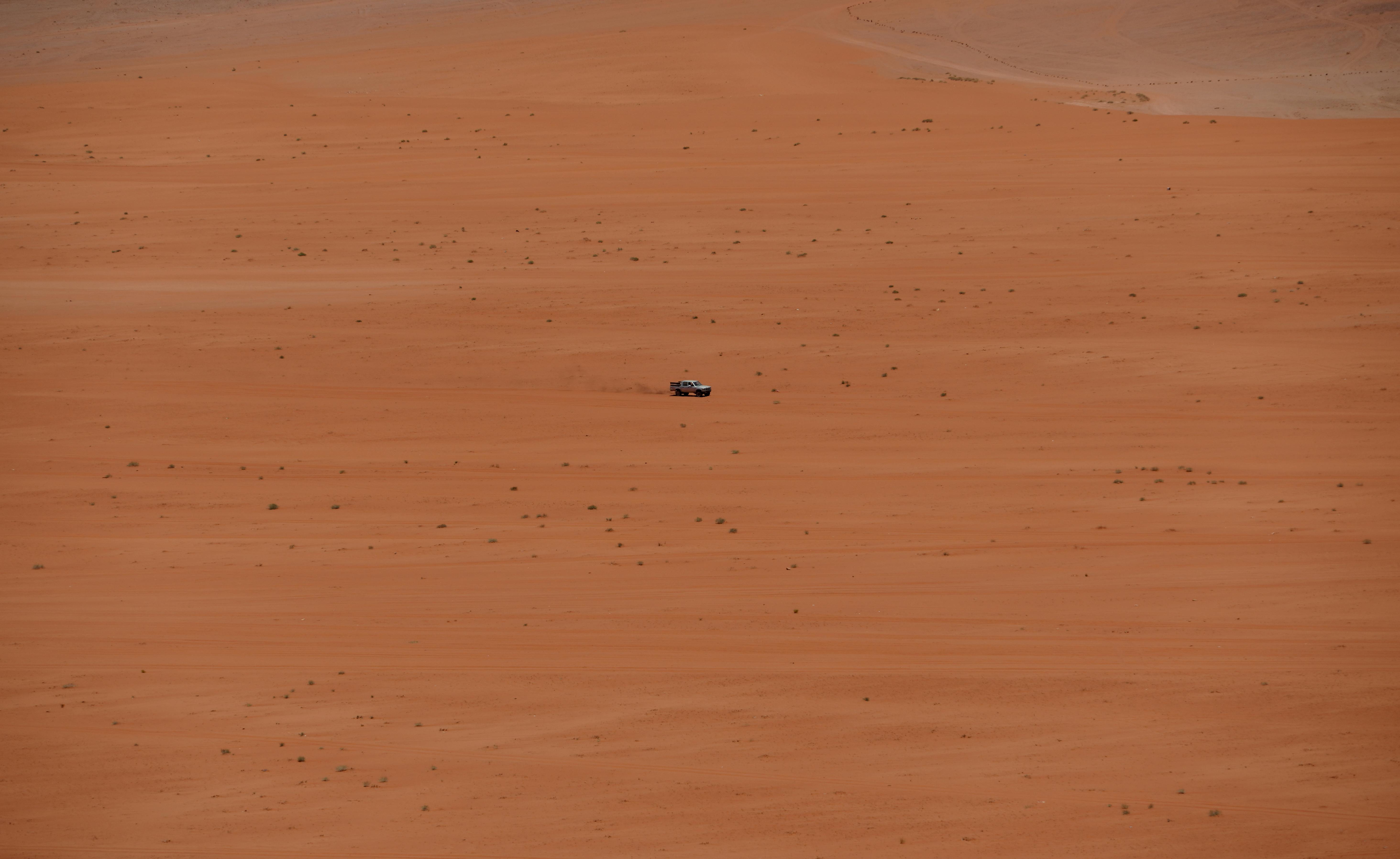 A lone vehicle traverses the vast sandy expanse of the Jordan desert, depicting isolation and adventure.