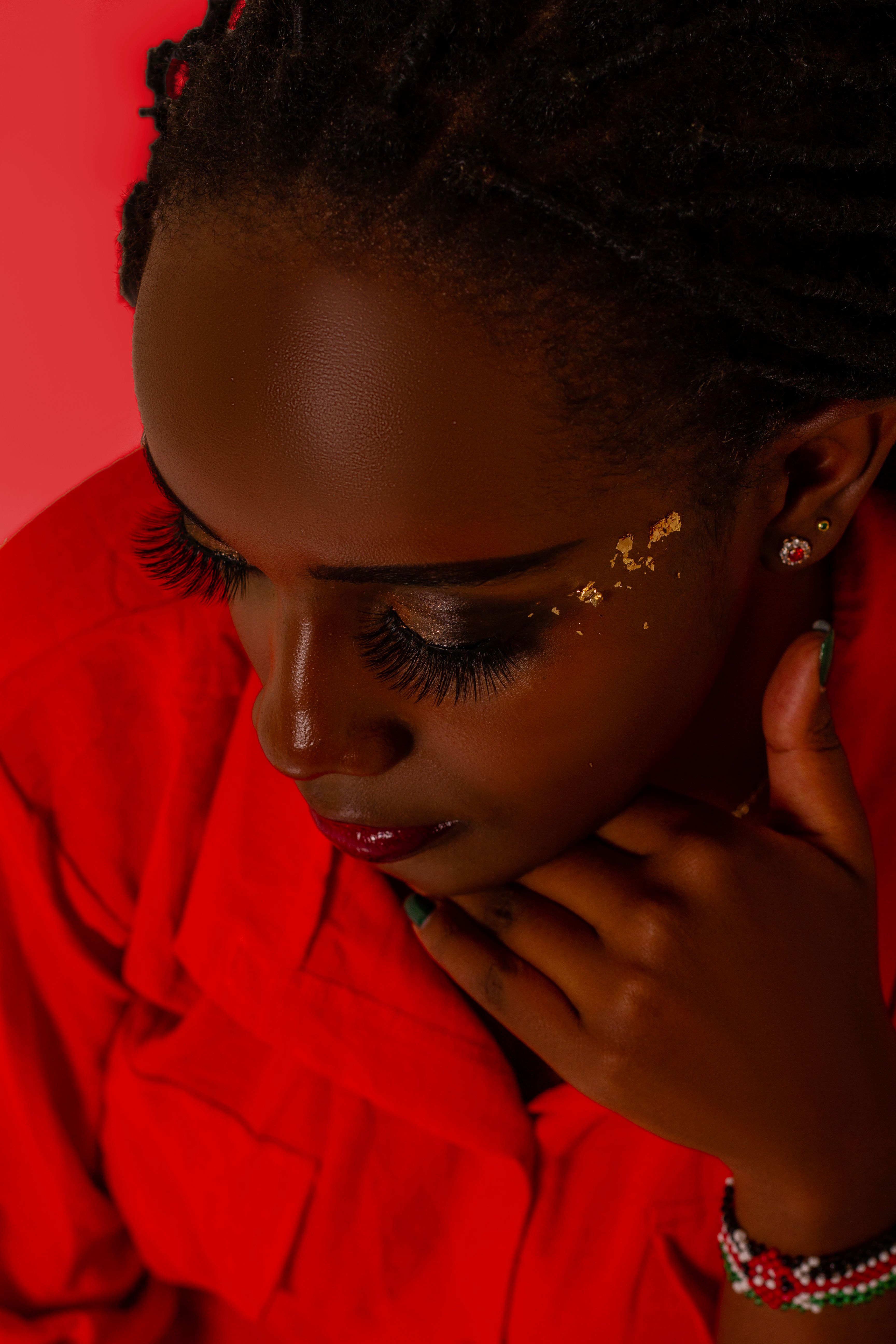 Stunning portrait of a woman with gold makeup accents against a vivid red background.