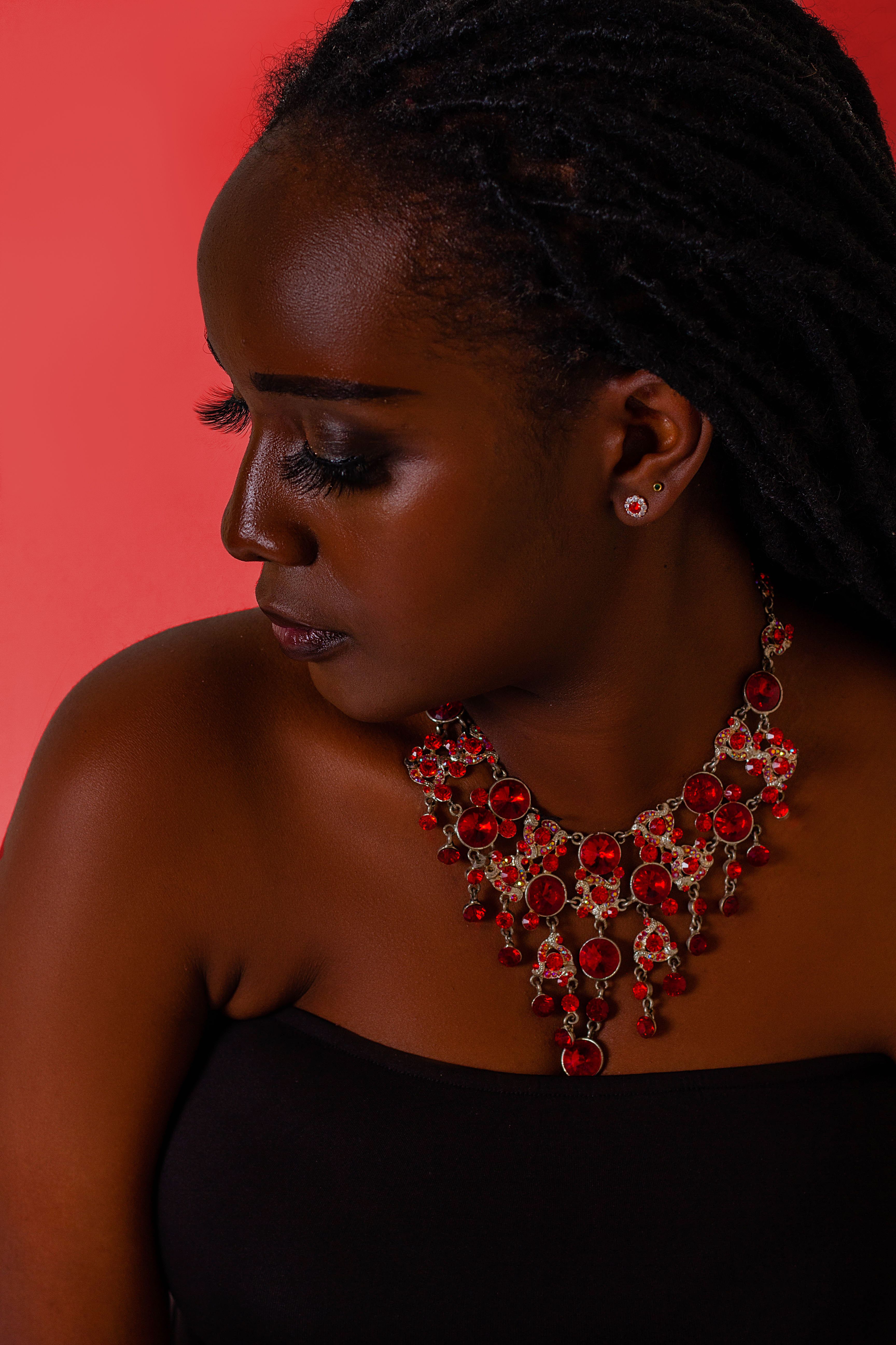 A striking portrait of a woman wearing a bold red gemstone necklace, set against a vibrant background.