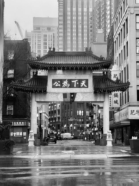 Black and white photo of a traditional Chinatown gate in an urban setting, conveying cultural heritage.