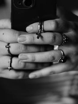 Black and white close-up of hands with rings holding a phone, artistic composition.