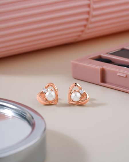 Rose-gold heart stud earrings with pearls on a pink background