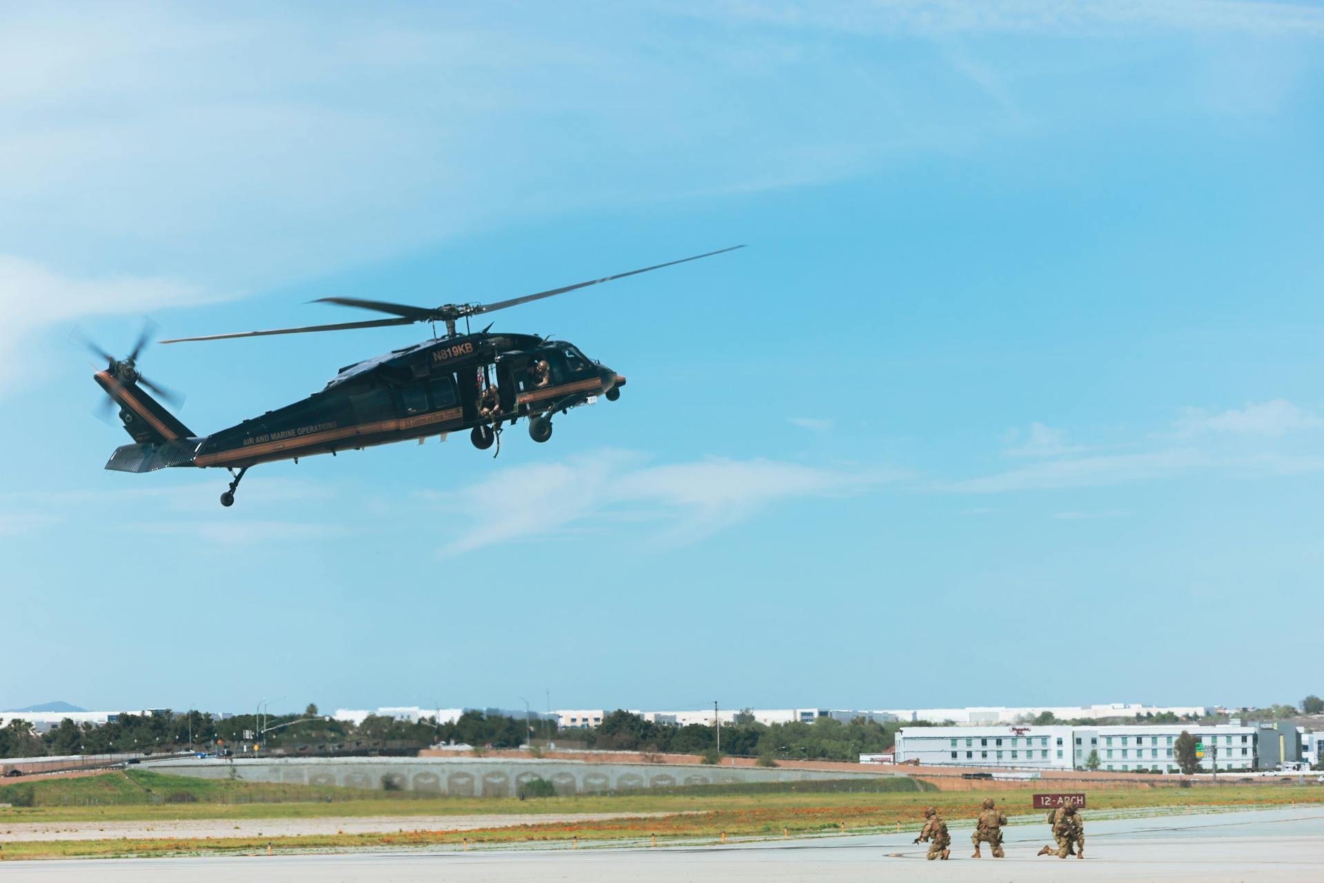 Black hawk helicopter hovering over an airfield with a clear blue sky, capturing military activity.