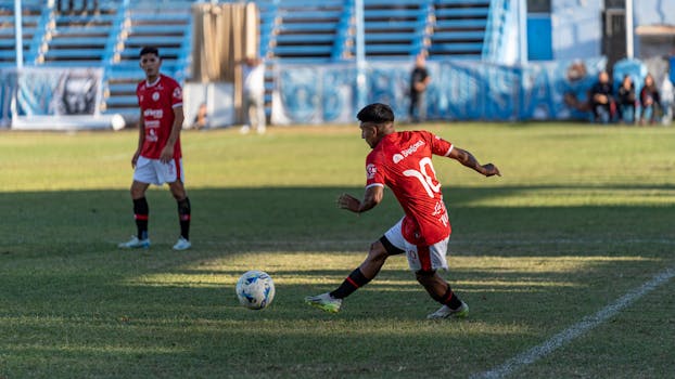 Player in red jersey kicking soccer ball during outdoor match.