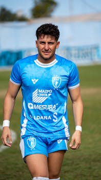 Young male soccer player smiling on the field, wearing a blue kit