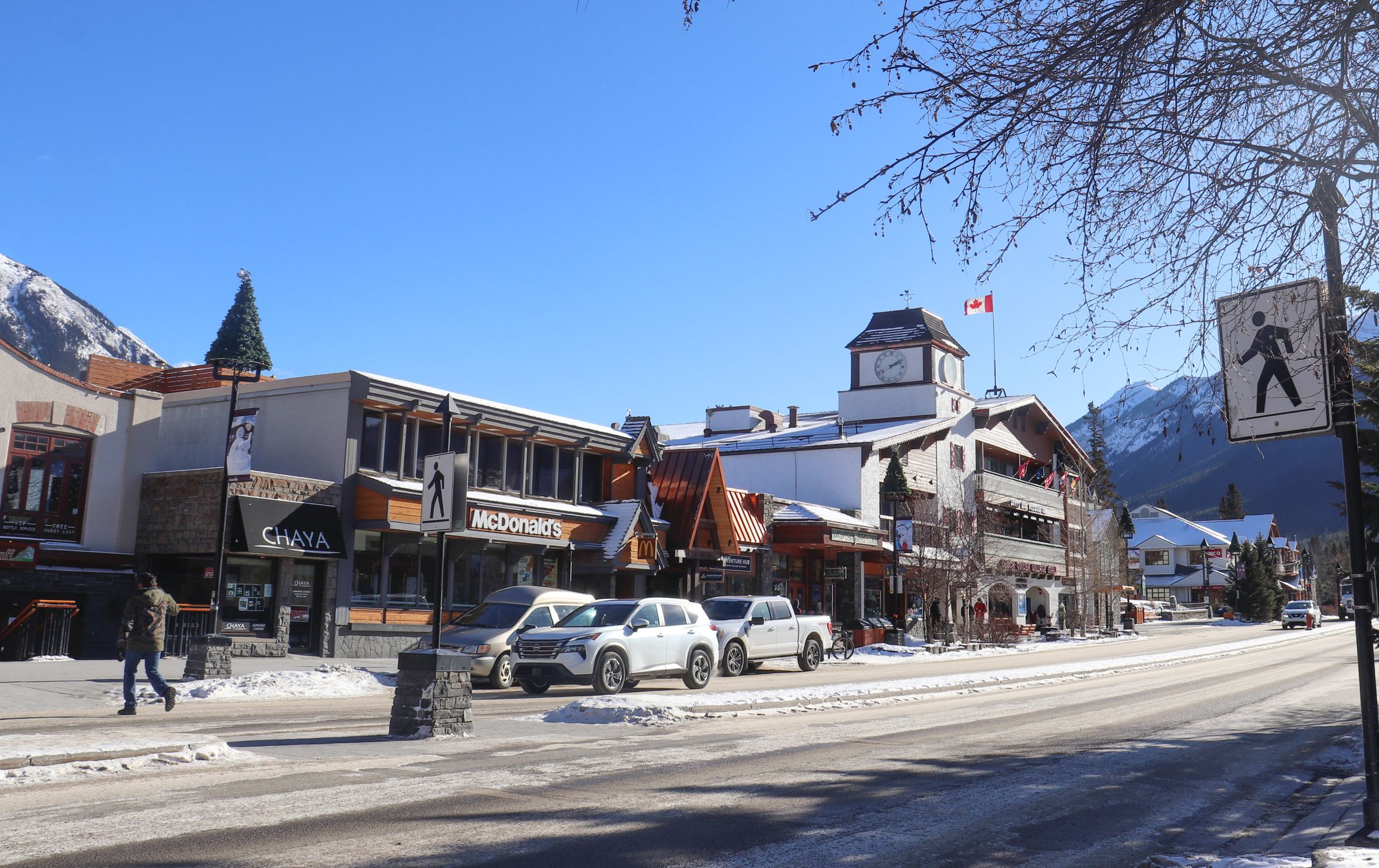 Scenic winter day on Banff Avenue, showcasing snowy streets, shops, and mountains.