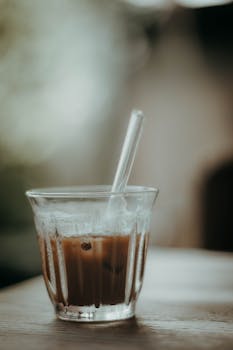 Aesthetic shot of iced coffee in a clear glass with straw on a wooden table.