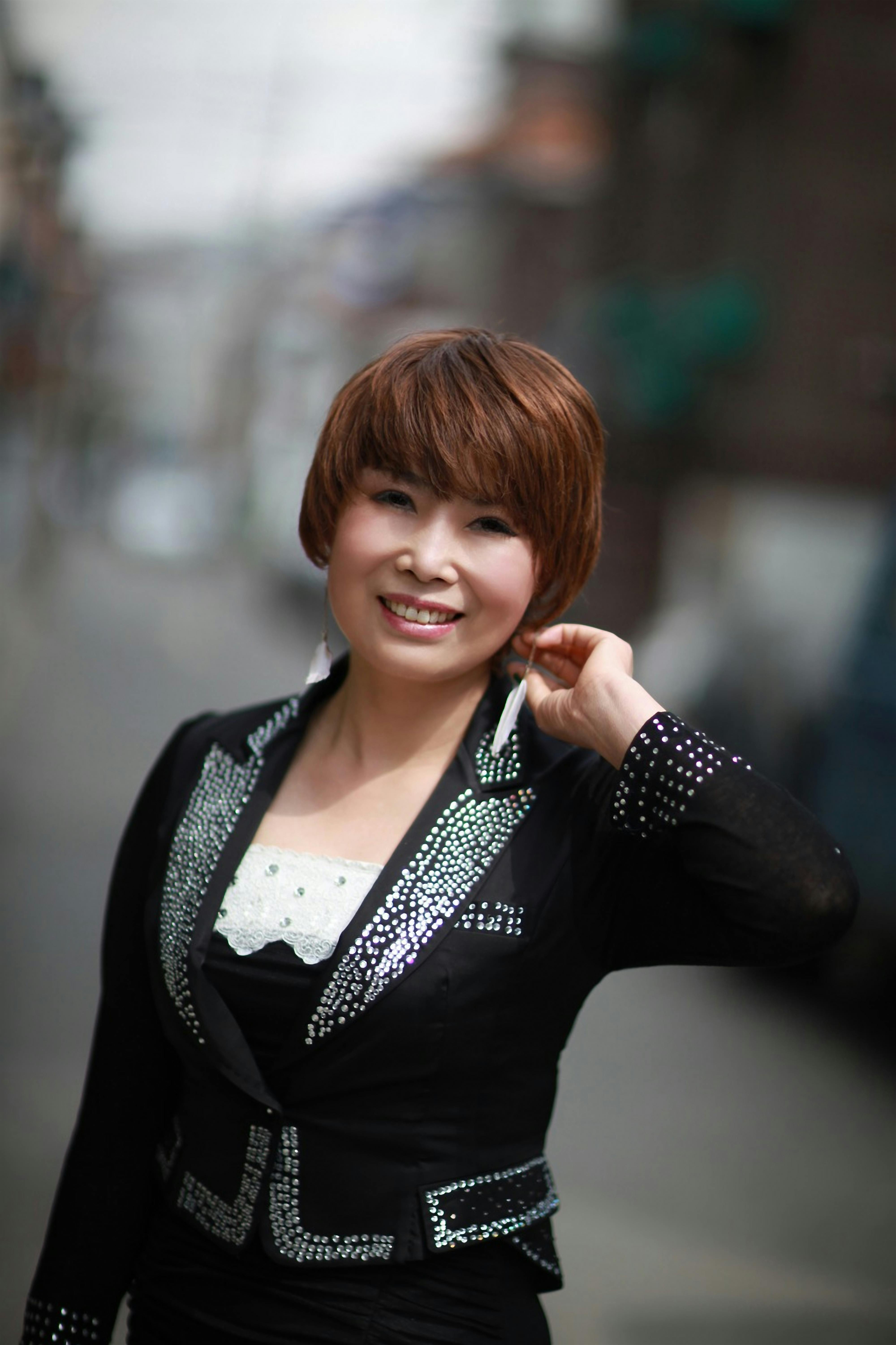 Smiling woman with short hair poses confidently in elegant attire on a city street.