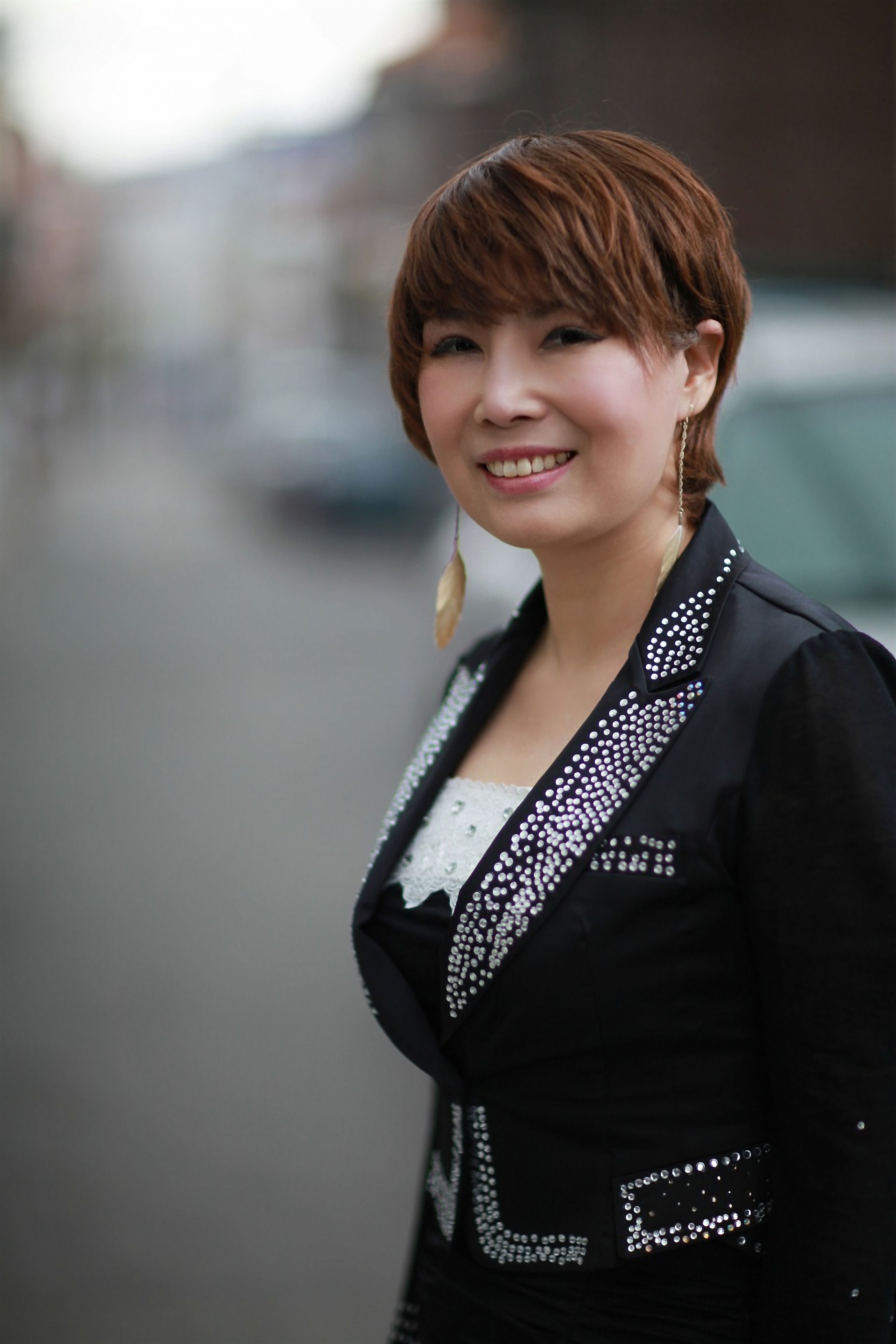Smiling woman in a stylish black outfit with rhinestones, posing outdoors.