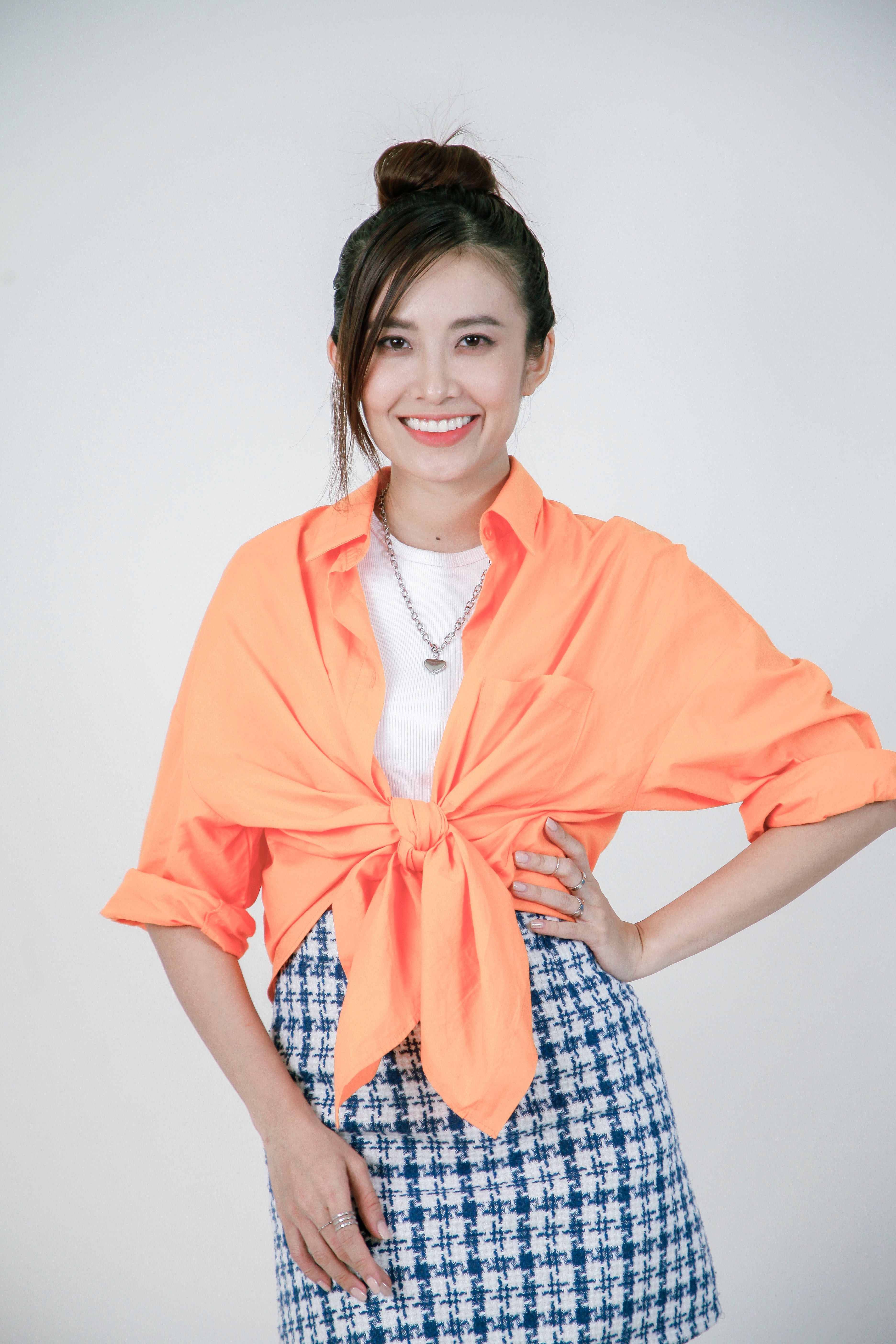 Smiling woman in vibrant orange top poses confidently indoors against a neutral background.