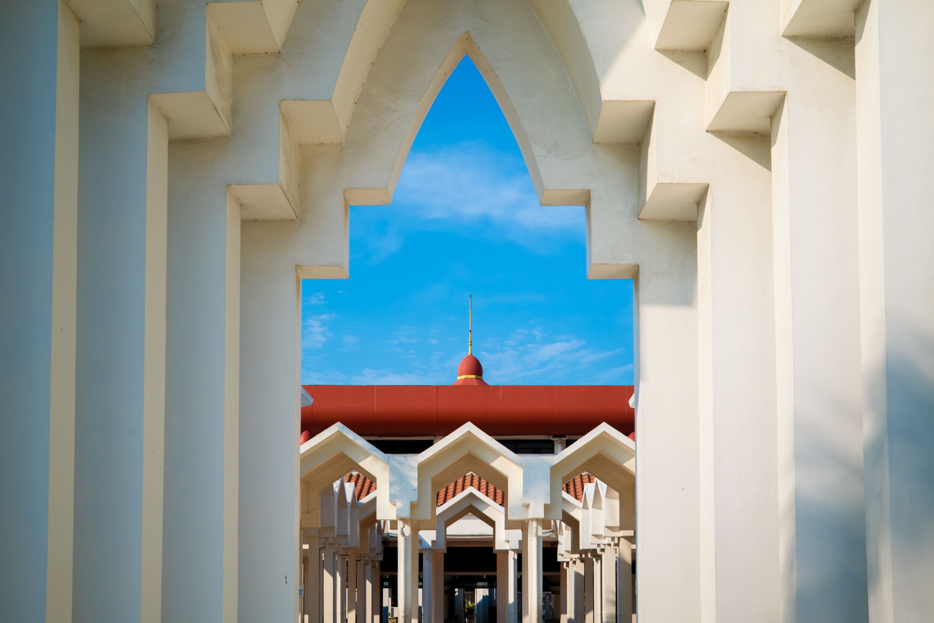Bright view of modern Islamic architectural elements at a mosque in Jakarta, Indonesia under a clear blue sky.