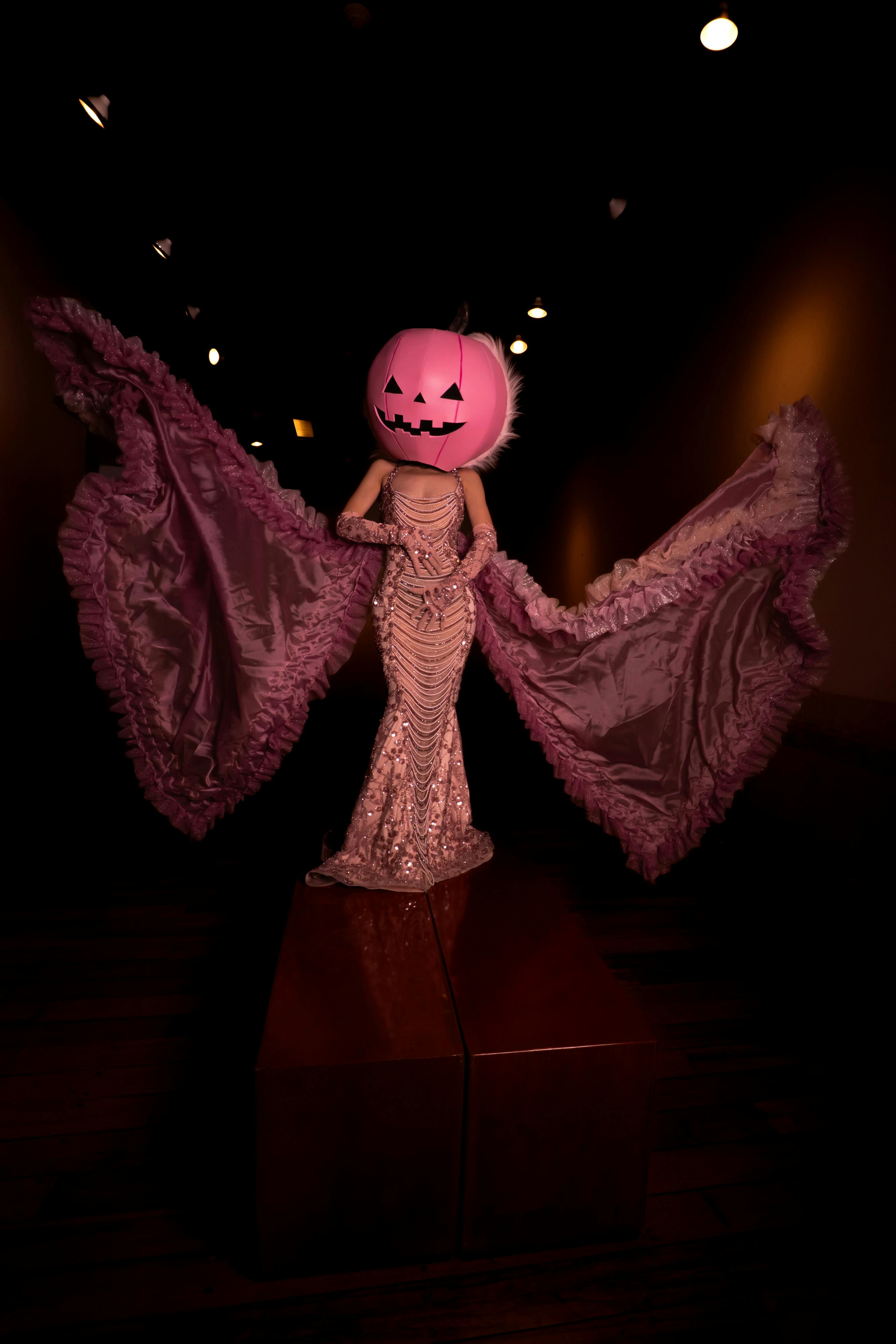 Free A dramatic Halloween costume featuring a pumpkin head and flowing gown in an indoor setting. Stock Photo