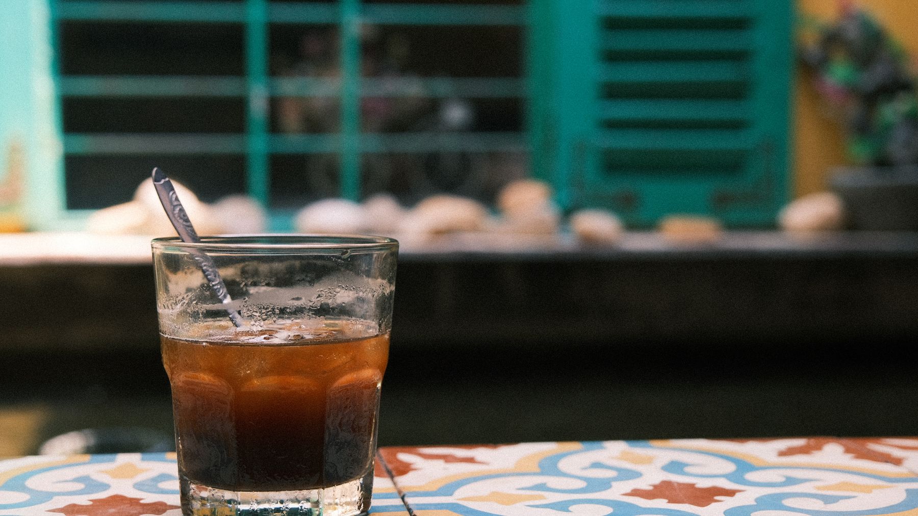 A refreshing glass of iced coffee with a spoon on a vibrant patterned table outdoors.