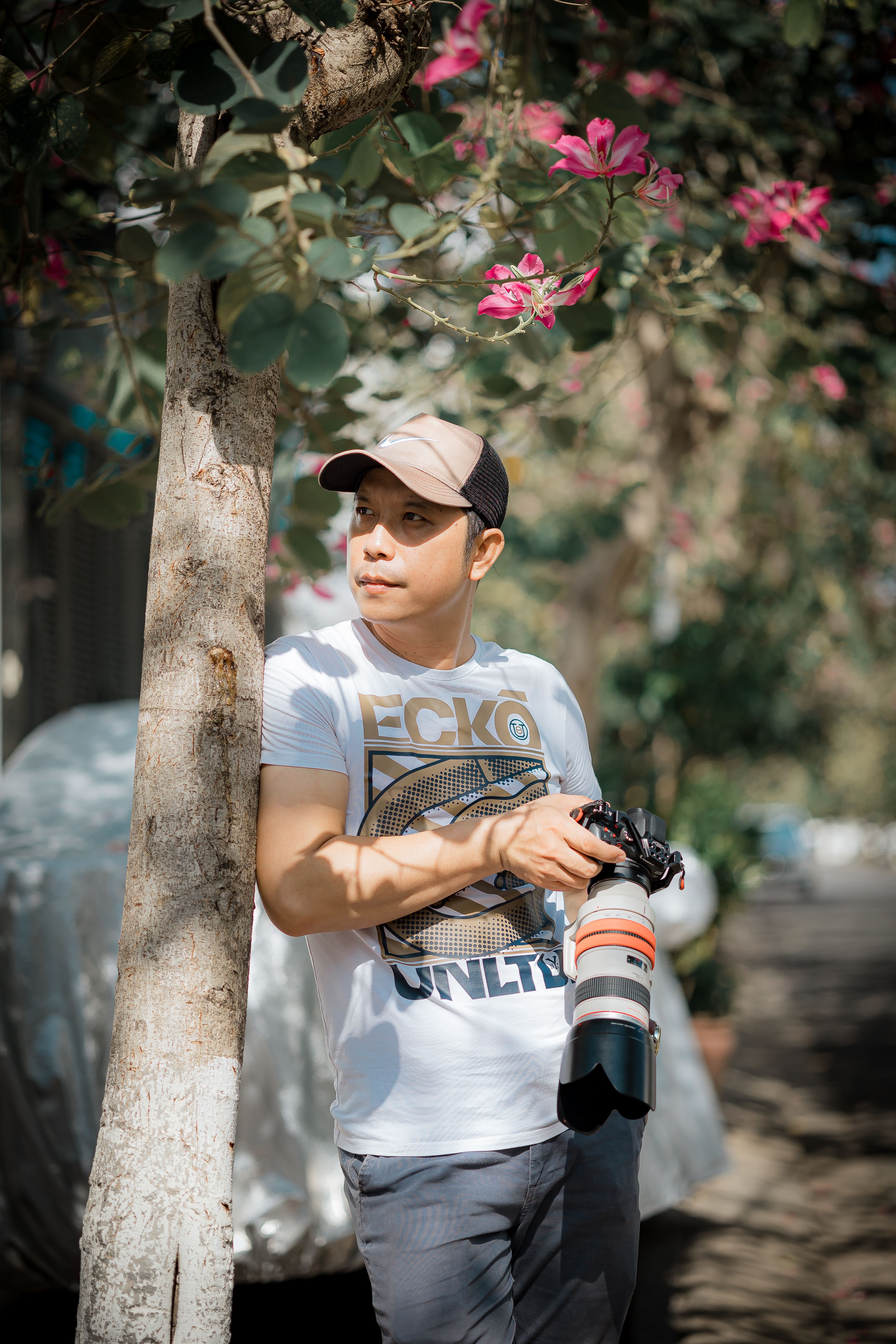 Casual photographer holding camera under a blooming tree, enjoying daylight.