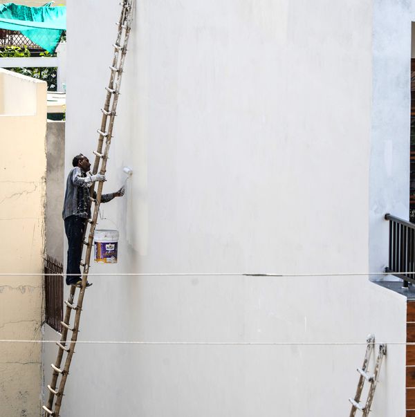 Painter on a ladder applying white paint to the exterior of a building.