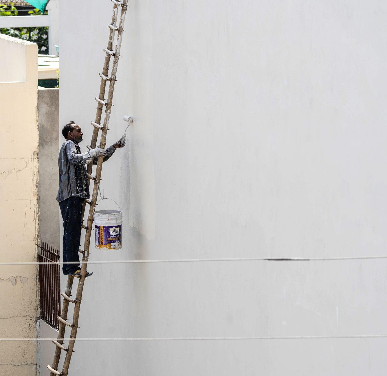 Painter on a ladder applying exterior coating to a wall with a roller — painting stucco with elastomeric paint in San Diego