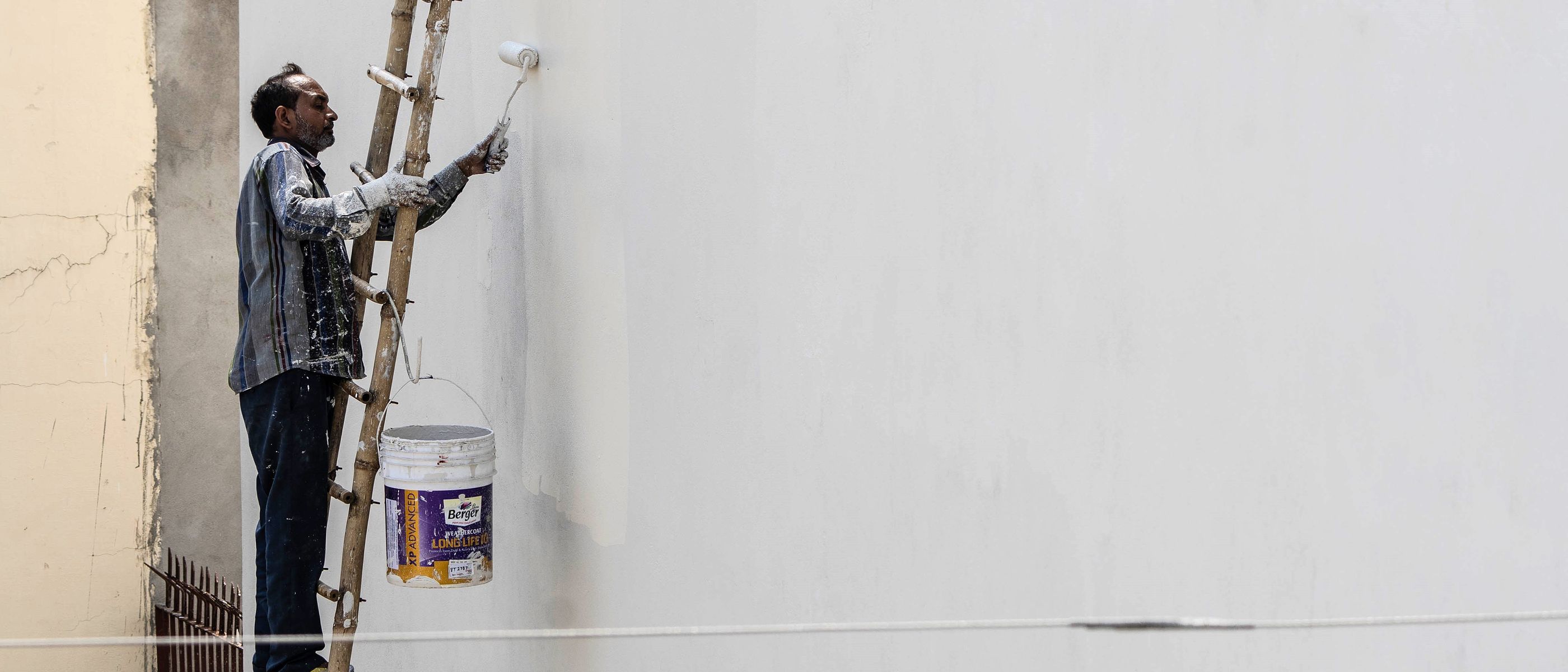 Painter on a ladder painting an exterior wall with a roller