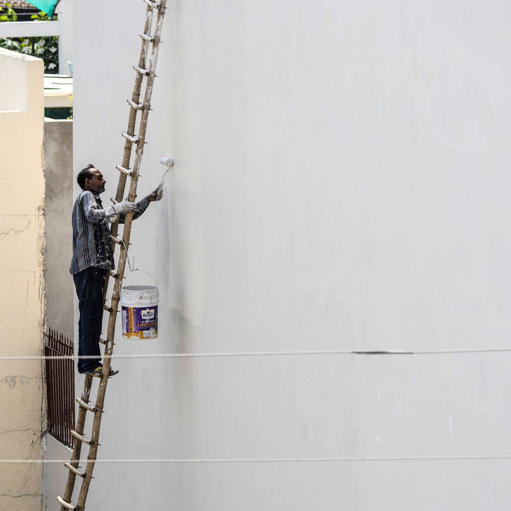 Painter on a ladder painting an exterior wall with a roller