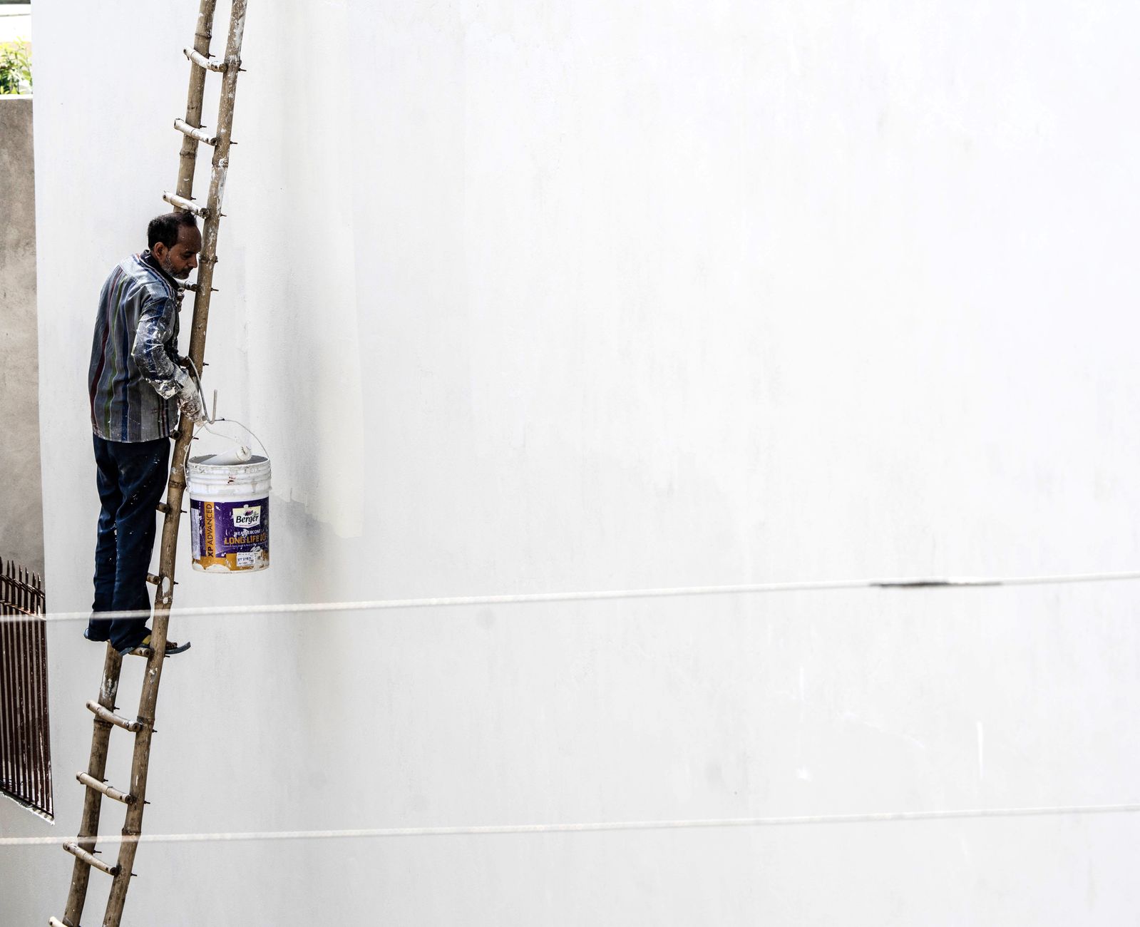 Worker on a ladder painting a large exterior wall — phased community association painting in San Diego County